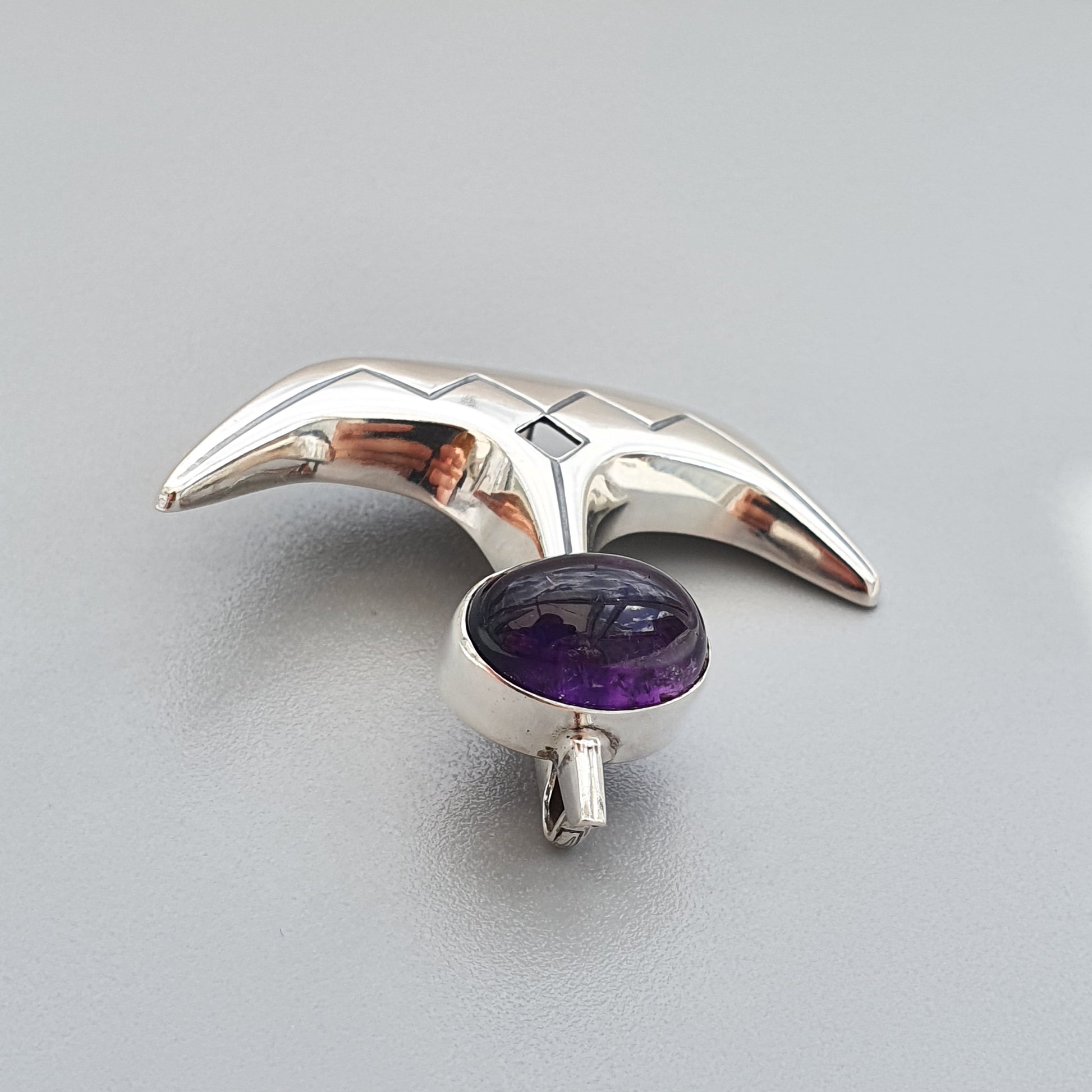 Silver brooch or pendant shaped like a bird in flight with a purple gemstone at its center.