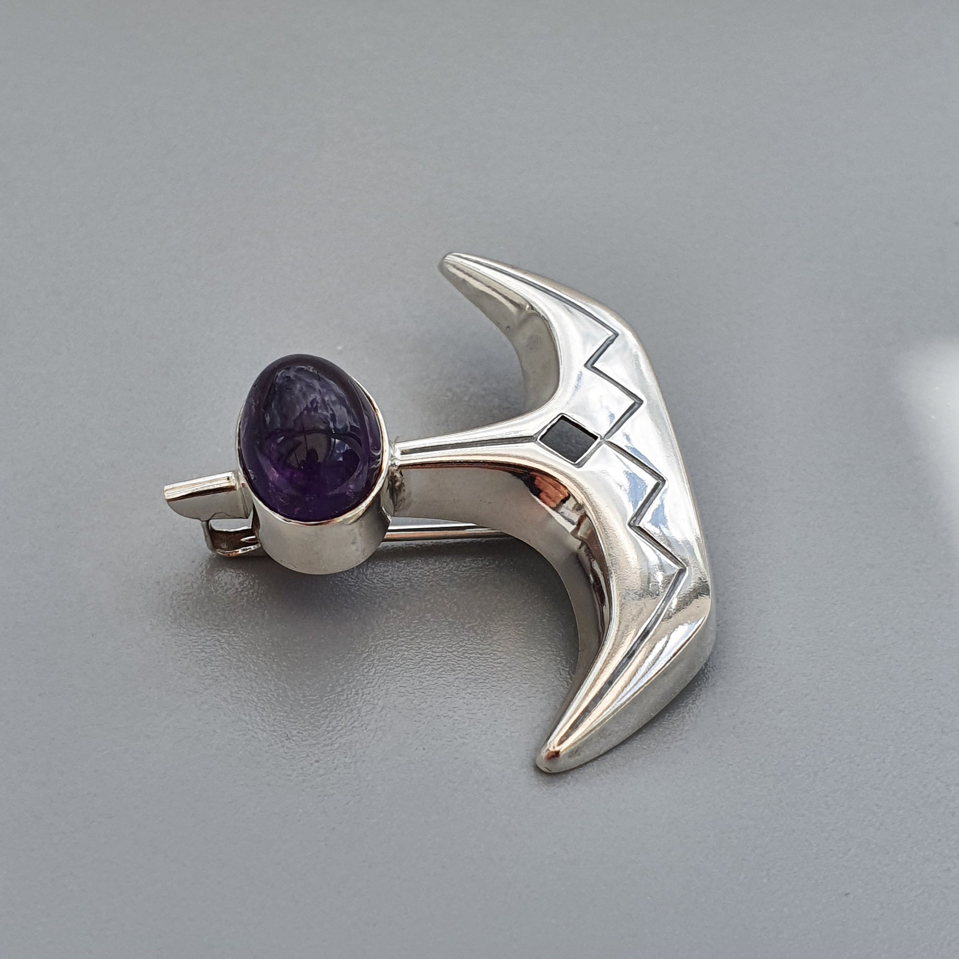 Silver anchor-shaped brooch or pin with a purple gemstone.