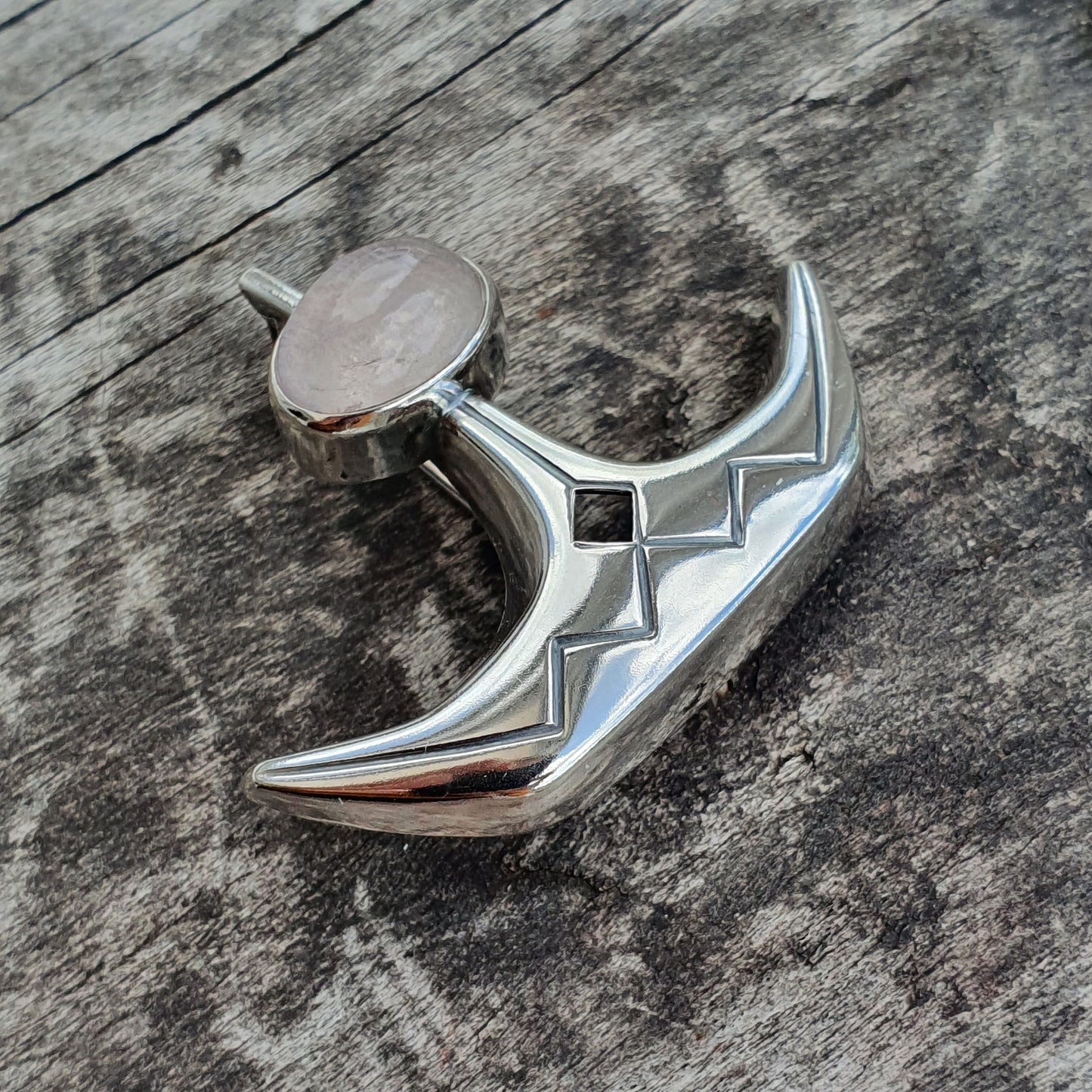 Shiny silver pendant or charm shaped like a crescent moon with geometric cutouts.