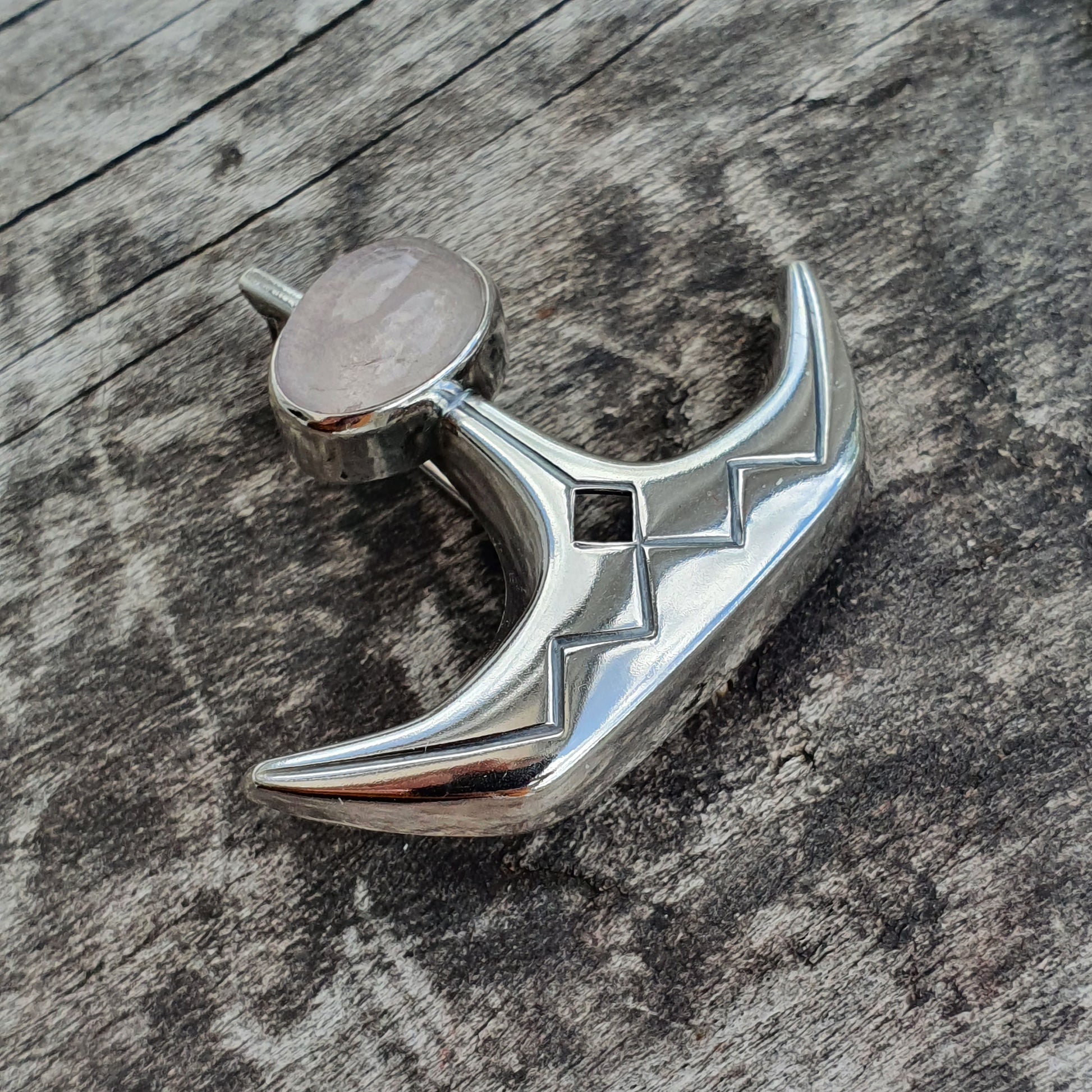 Shiny silver pendant or charm shaped like a crescent moon with geometric cutouts.