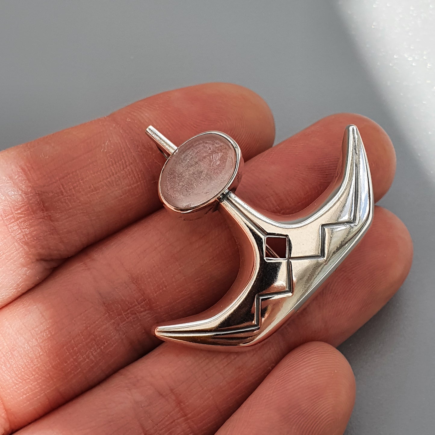 Silver pendant or charm shaped like a stylized crescent moon with a circular element at the top.