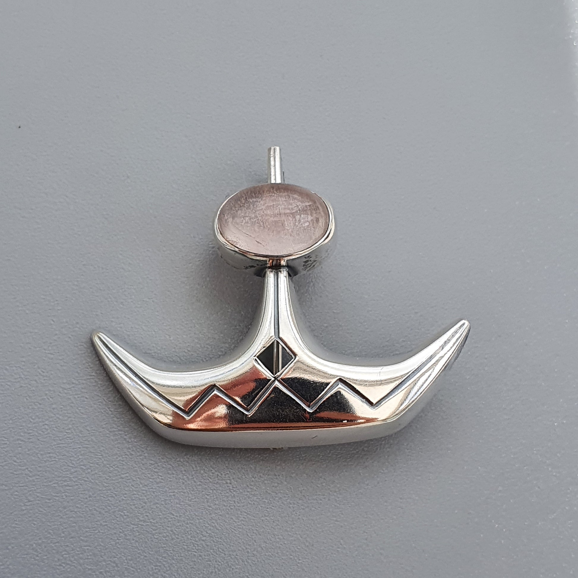 Silver pendant shaped like a stylized boat or ship’s hull with a circular gemstone at the top.