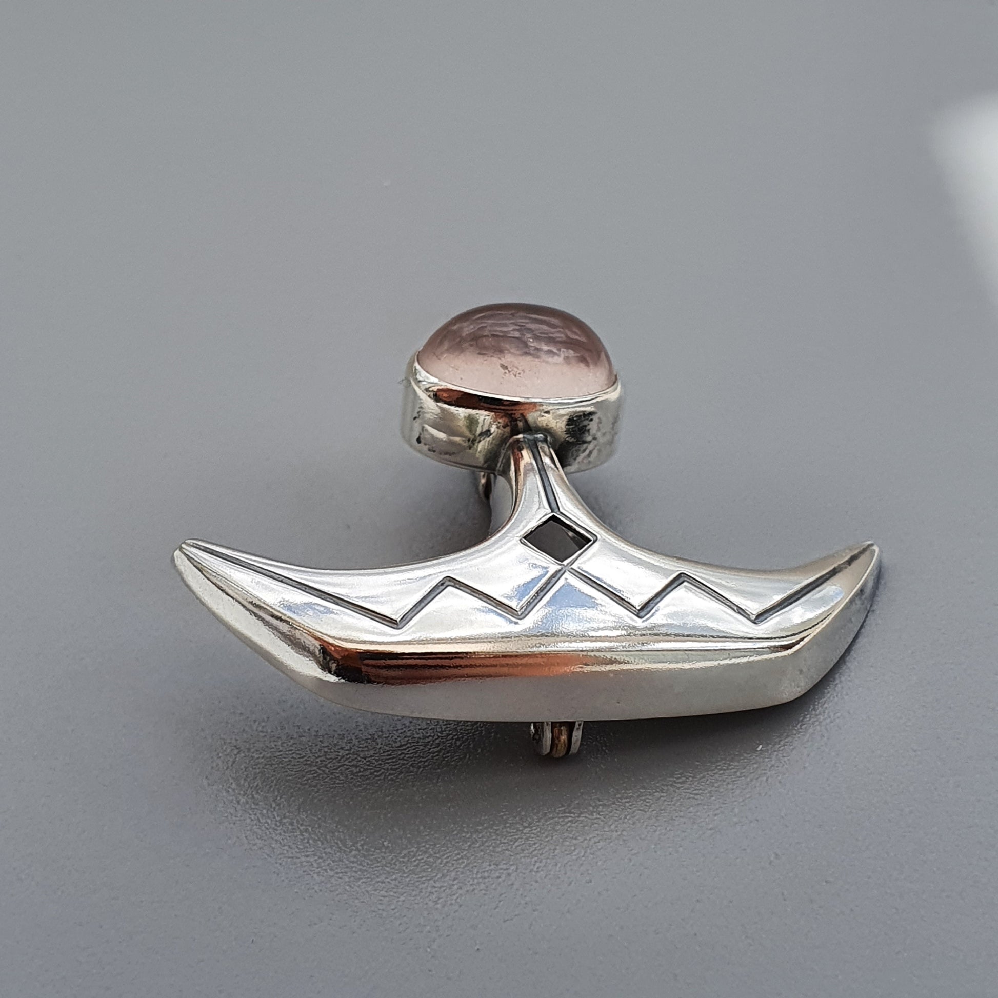 Silver brooch or pendant shaped like a stylized boat with a round gemstone at the top.