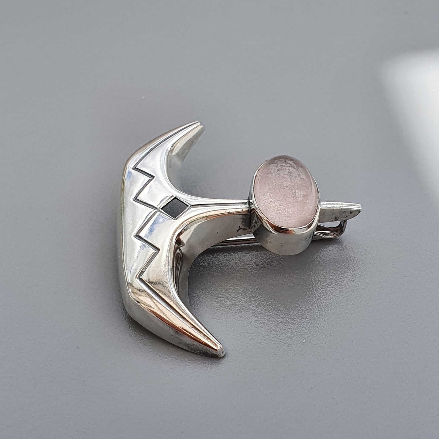 Crescent moon-shaped silver brooch or pin with a pale pink gemstone.