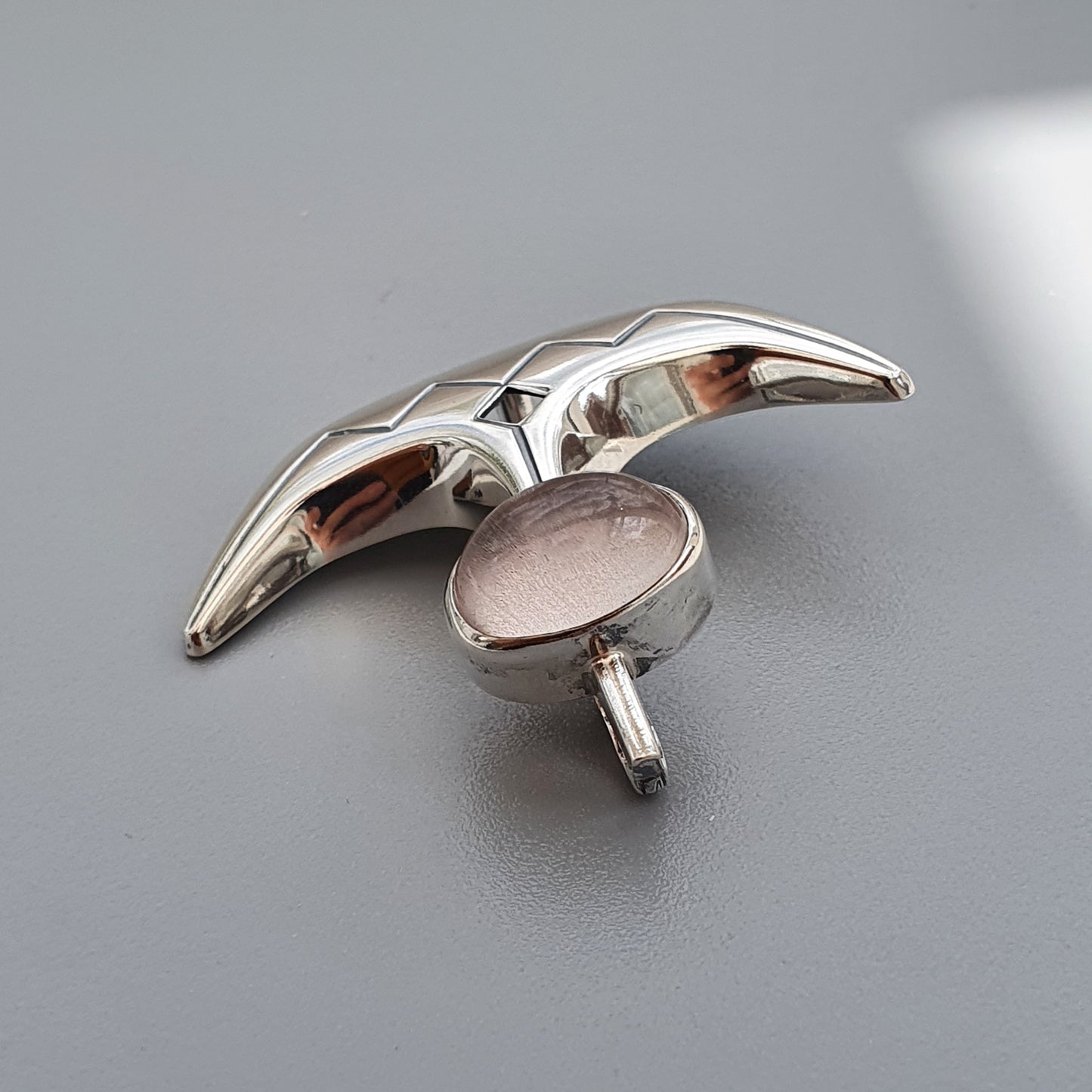 Silver cufflink shaped like a boomerang or curved wing.