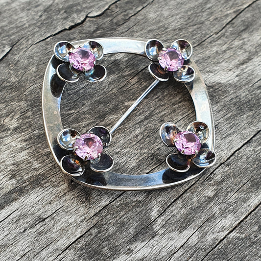 Silver brooch with four flower-shaped designs featuring pink gemstones.