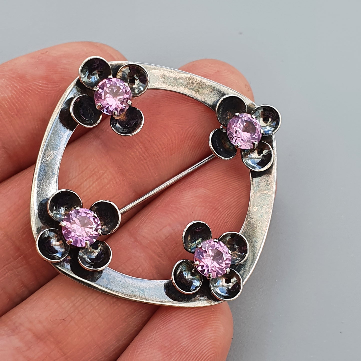 Silver brooch with four flower-shaped designs featuring pink gemstones.