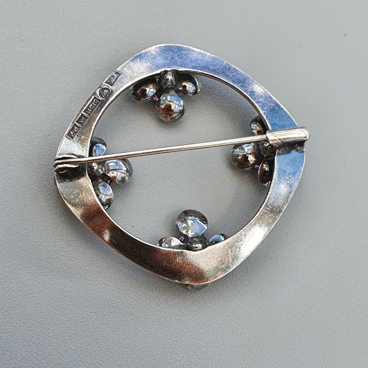 Silver circular brooch with small metallic spheres arranged around its perimeter.