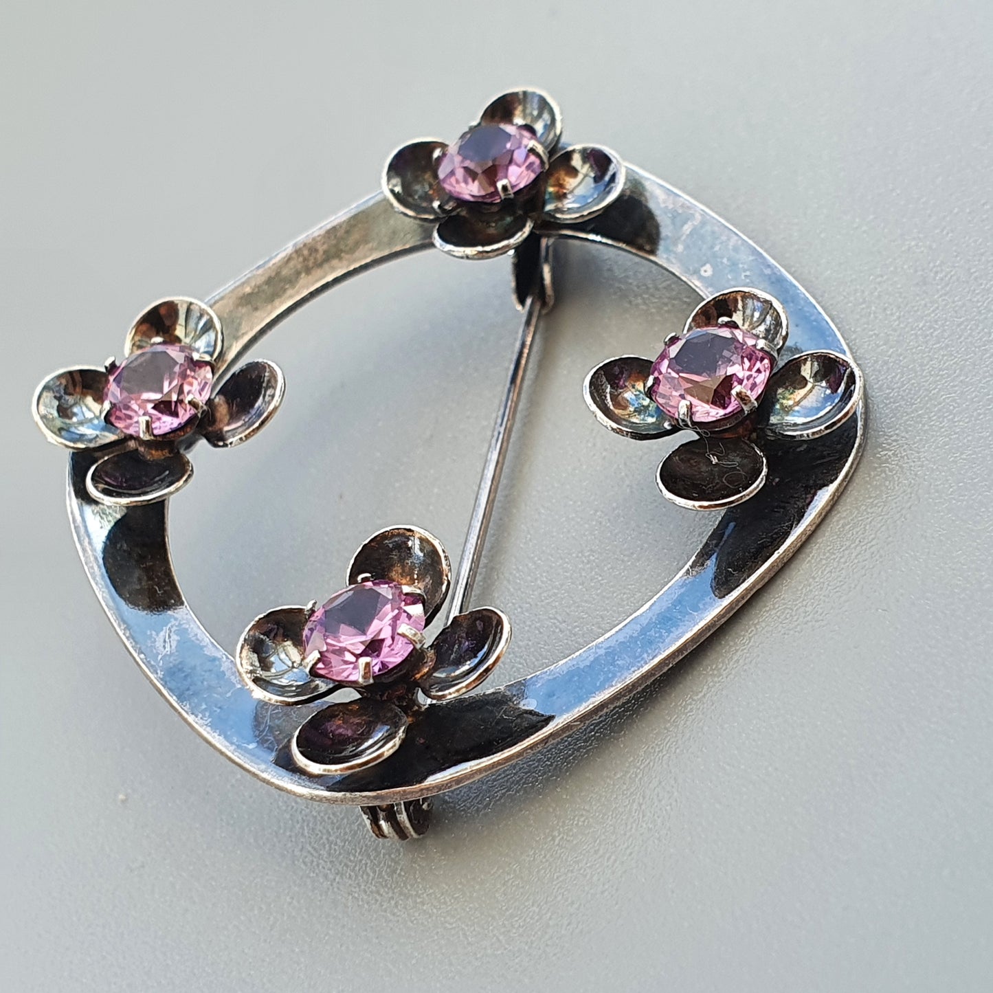 Silver brooch with four flower-shaped designs featuring pink gemstones.