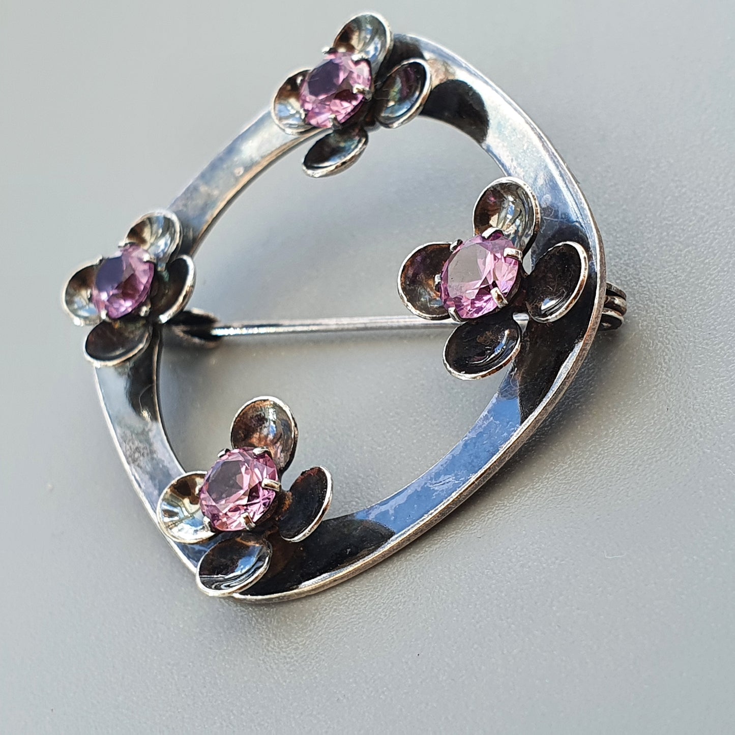 Silver brooch with four flower-shaped designs featuring pink gemstones.