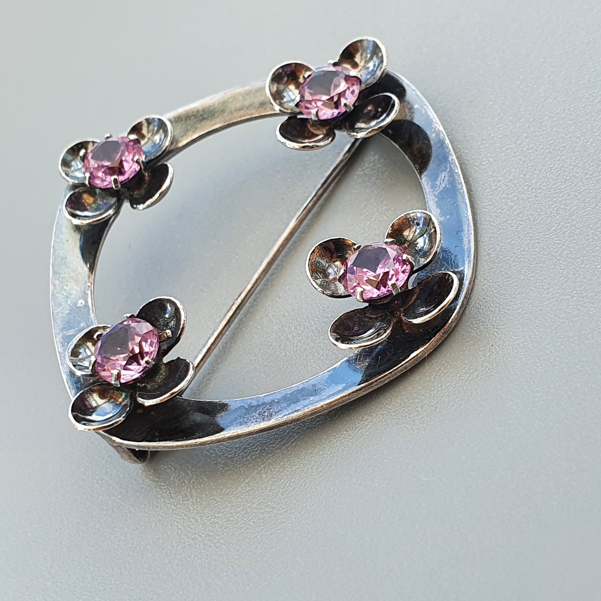 Silver brooch with four flower-shaped designs featuring pink gemstones.