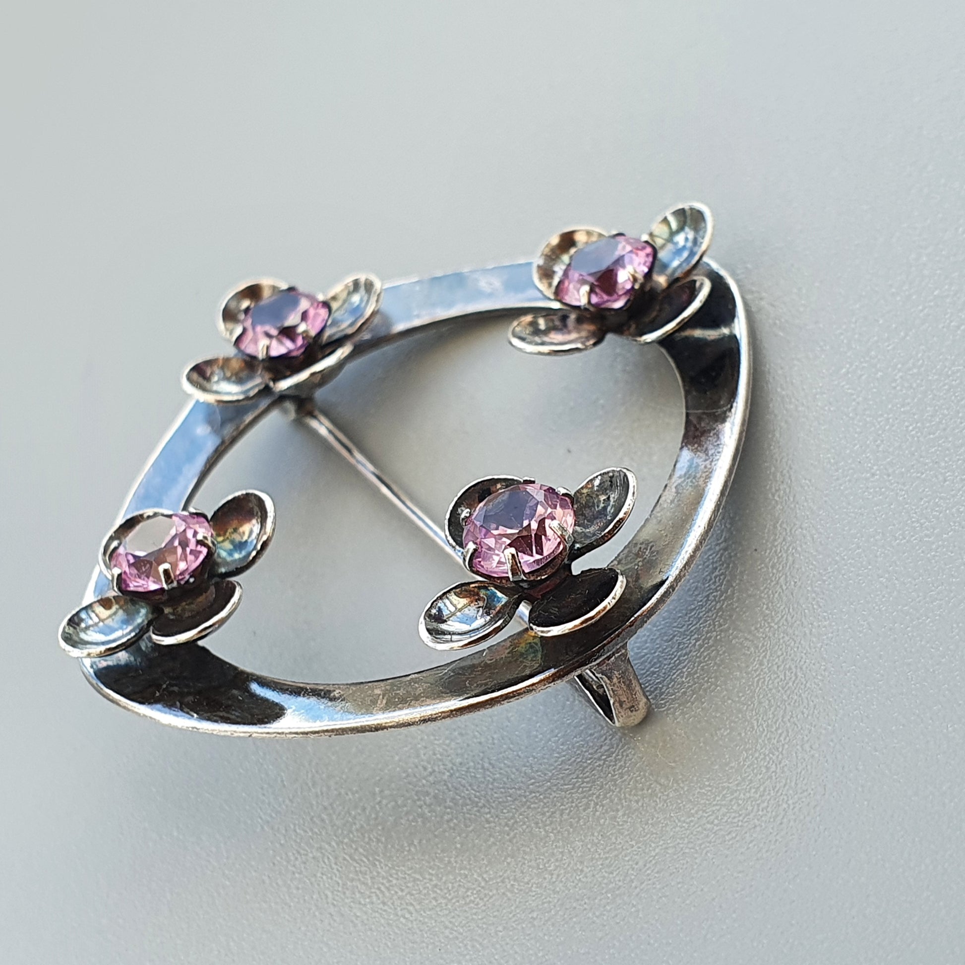 Silver brooch with four pink gemstones set in floral-like designs around an oval shape.