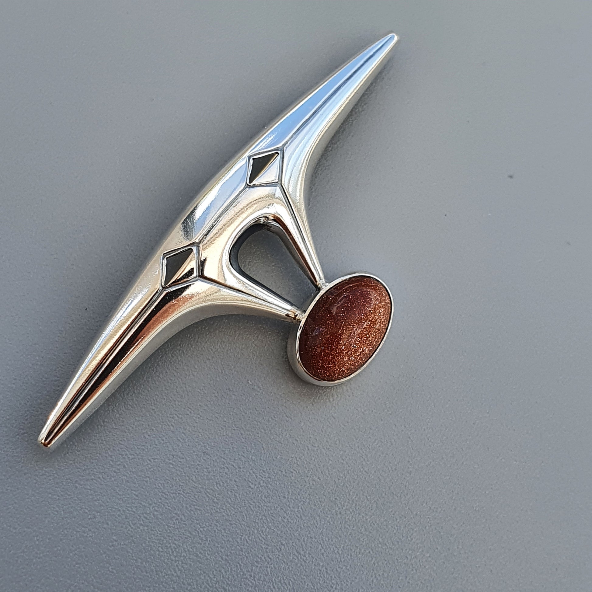 Sleek, modernist silver brooch with an elongated point and a round goldstone accent.