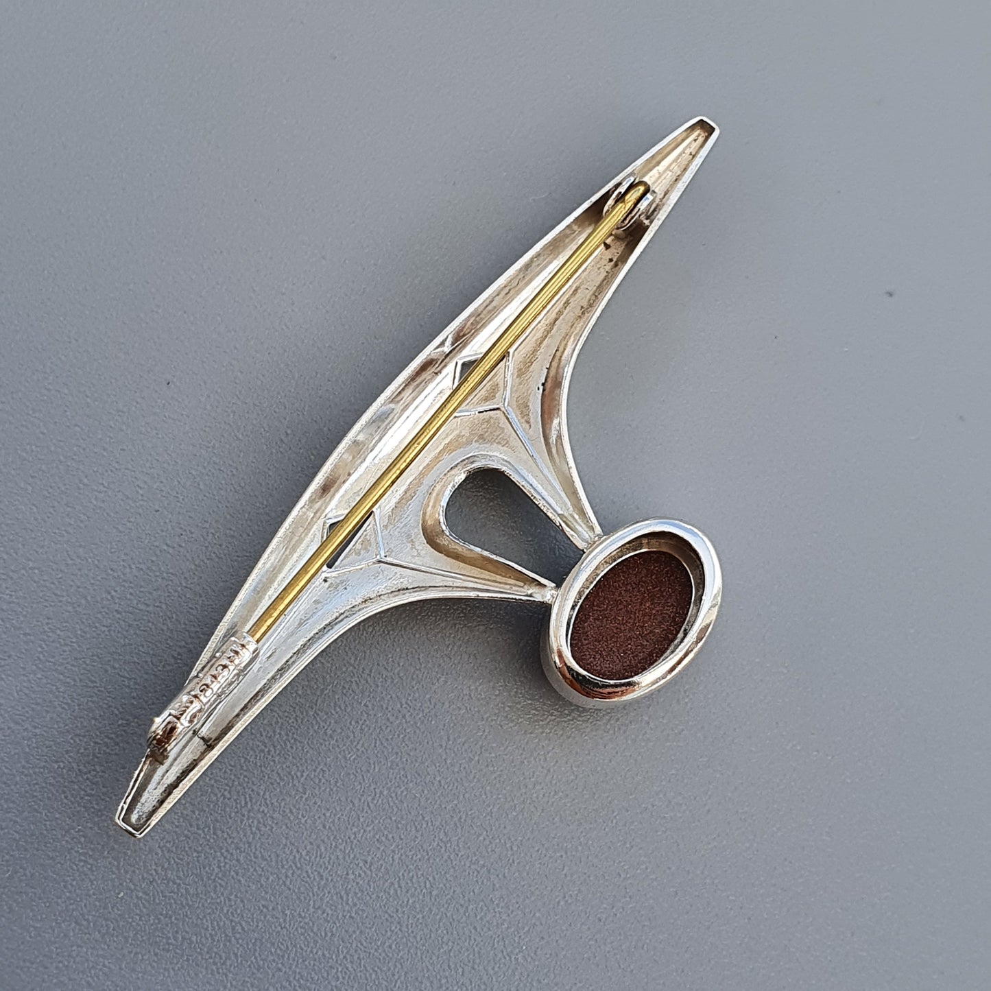 Metallic clothes pin or clamp with a unique geometric design and a circular brown pad.