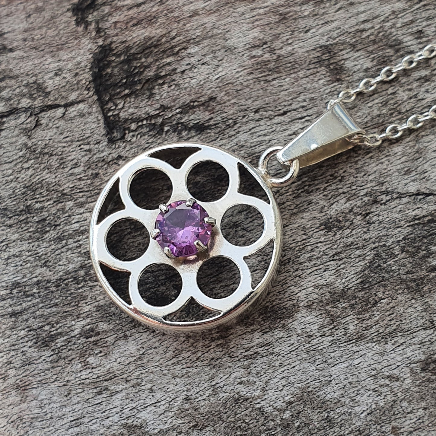 Silver pendant necklace featuring a circular design with multiple openings and a central purple gemstone.