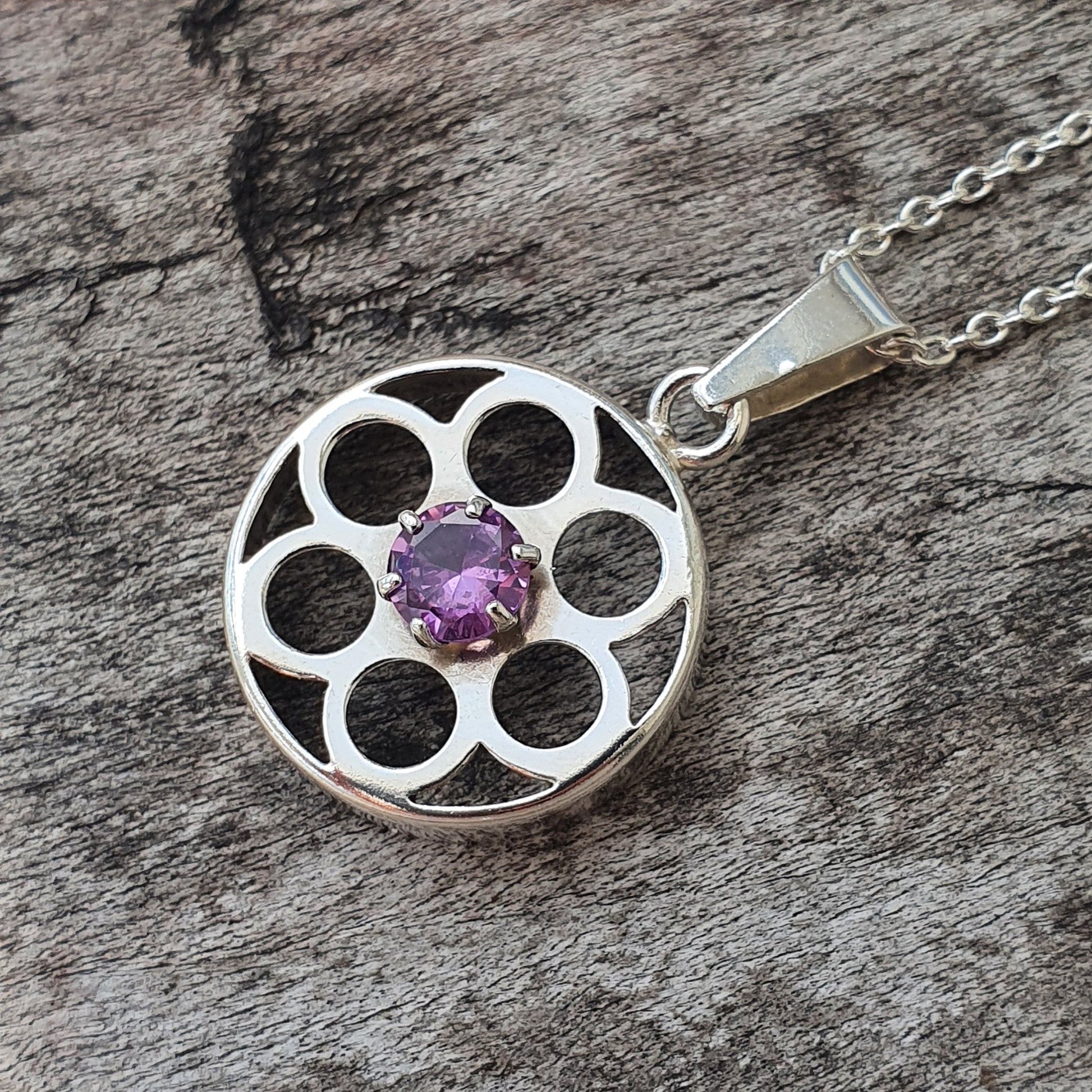 Silver pendant necklace featuring a circular design with multiple openings and a central purple gemstone.