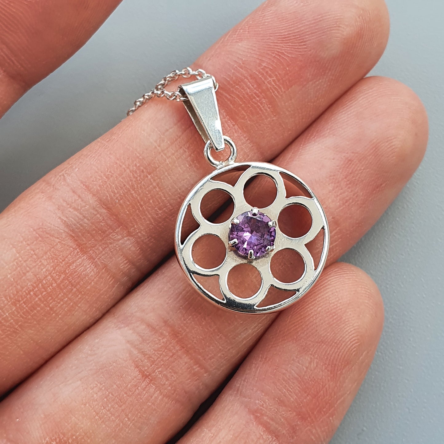 Silver pendant with a circular floral design and a purple gemstone in the center.