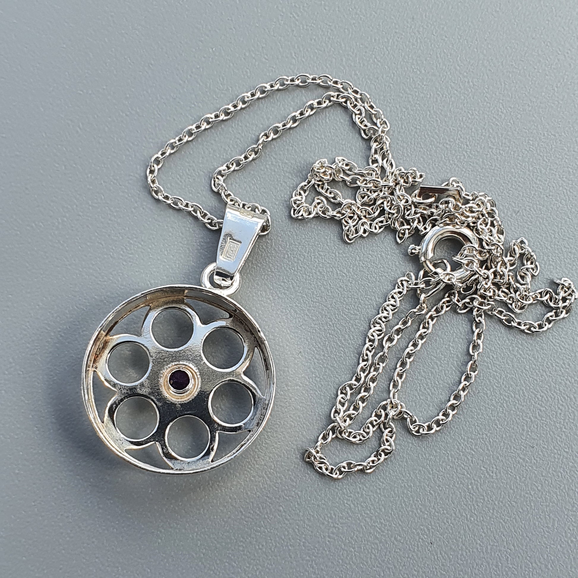 Silver pendant necklace with a circular charm featuring multiple circular cutouts.