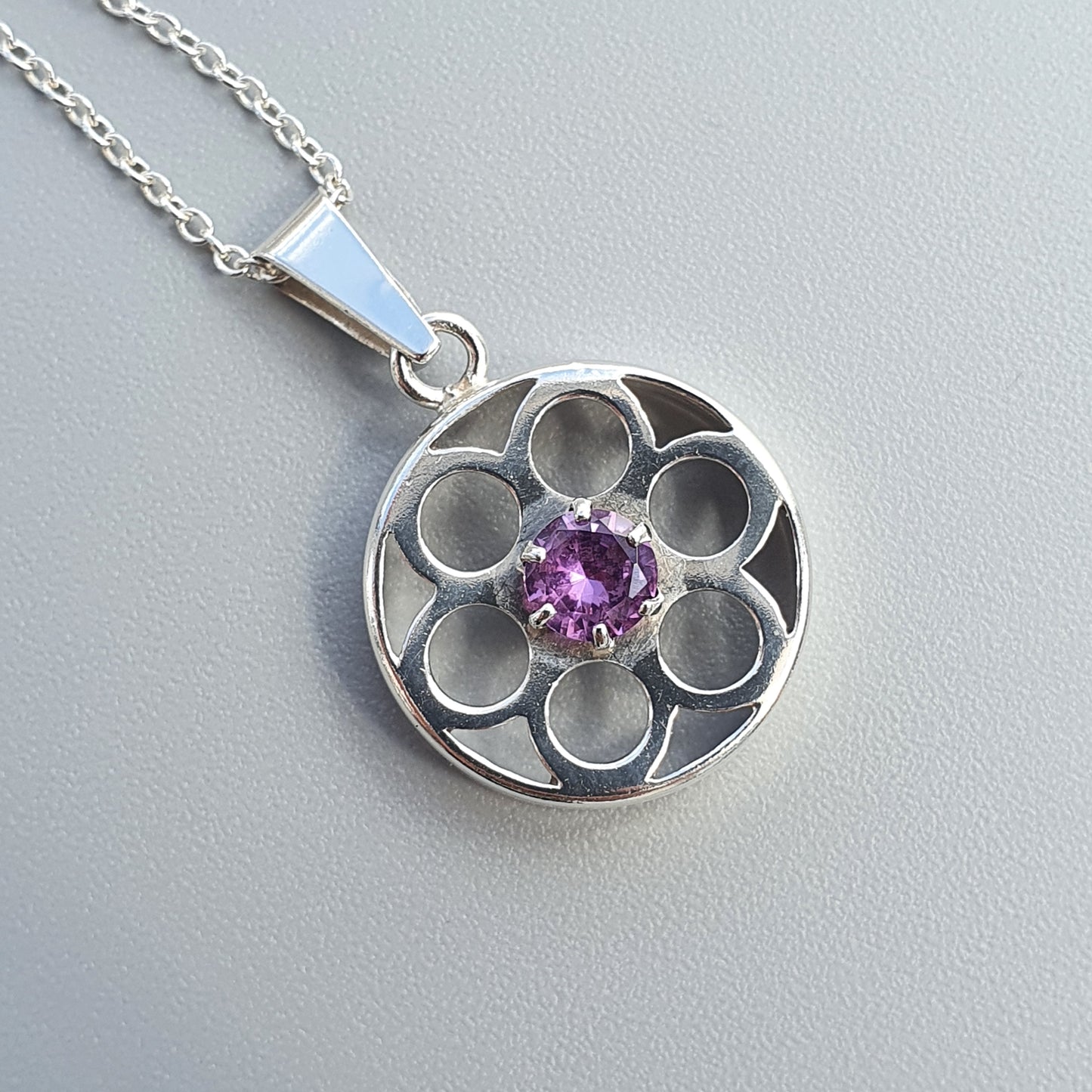 Silver pendant necklace with a circular floral design and purple gemstone center.