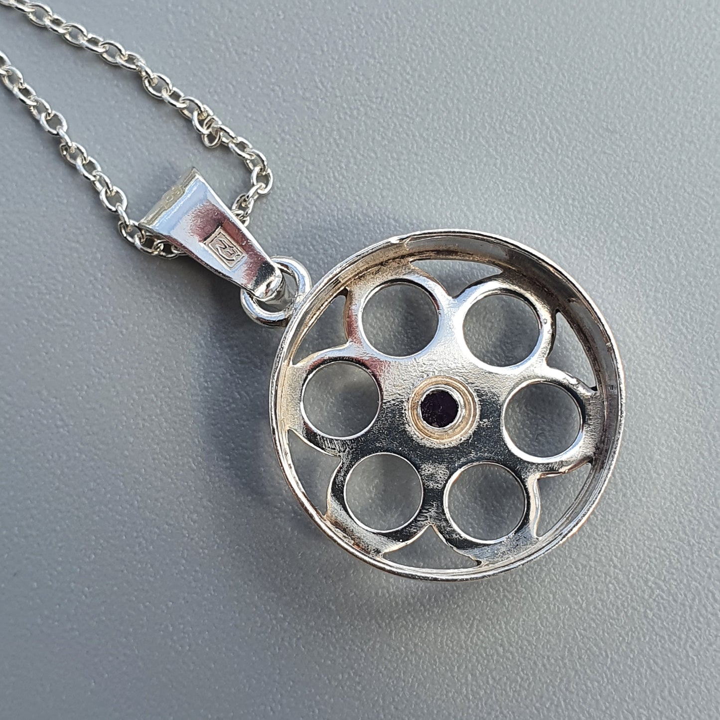 Silver pendant necklace featuring a circular charm with six holes arranged around a central hole.