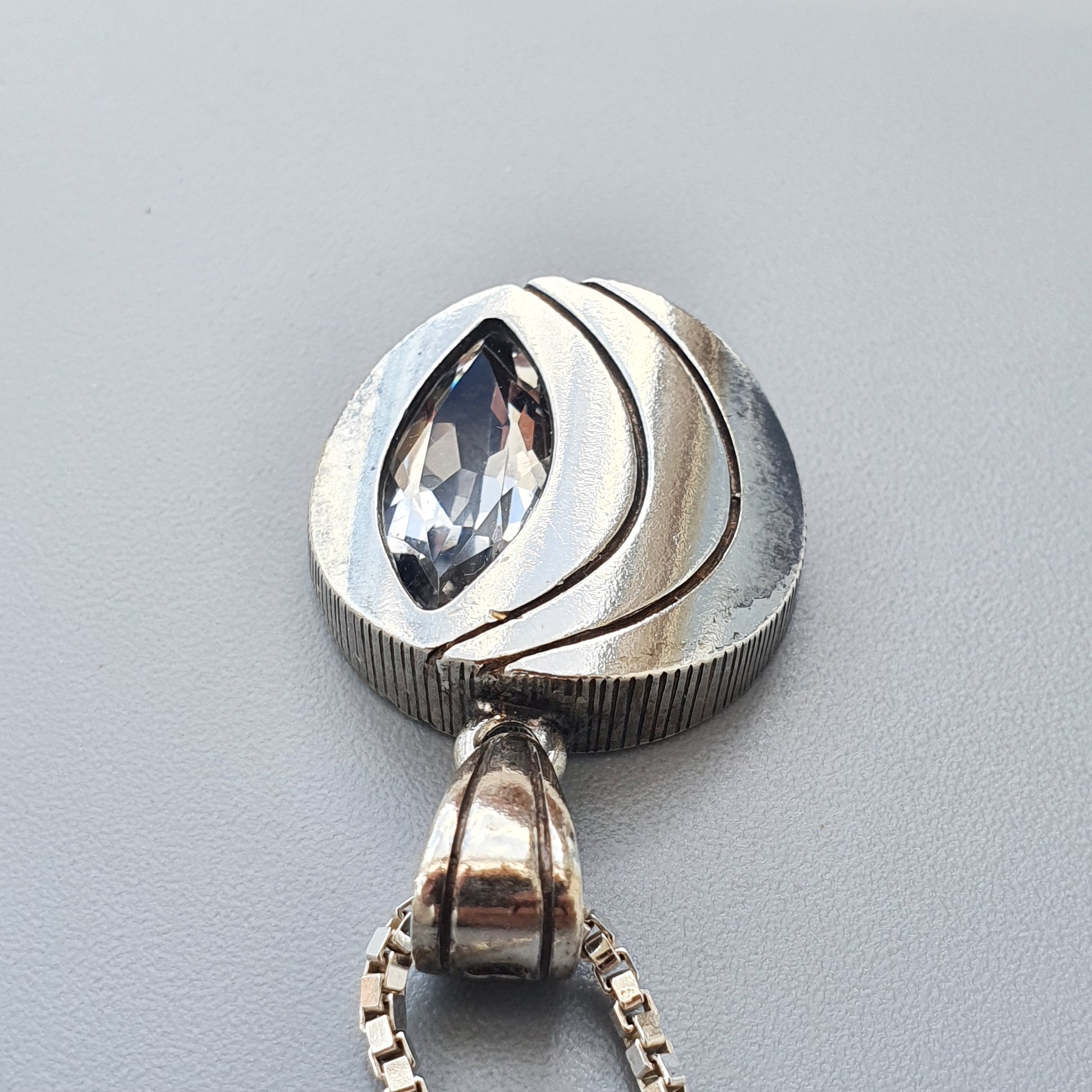 Silver pendant featuring a marquise-cut gemstone set in a swirling, modernist design.