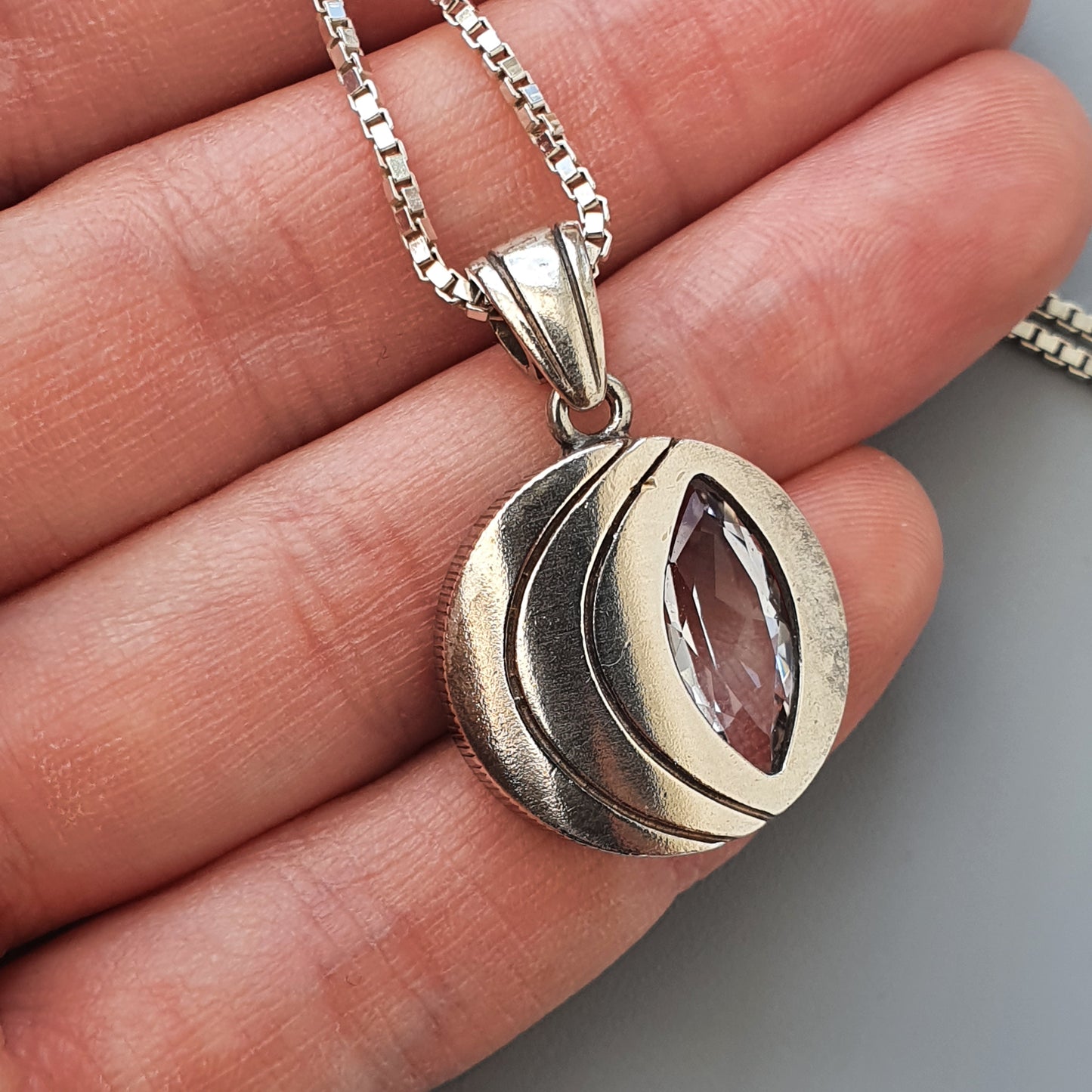 Silver pendant necklace with a marquise-cut purple gemstone in a stylized leaf or petal design.