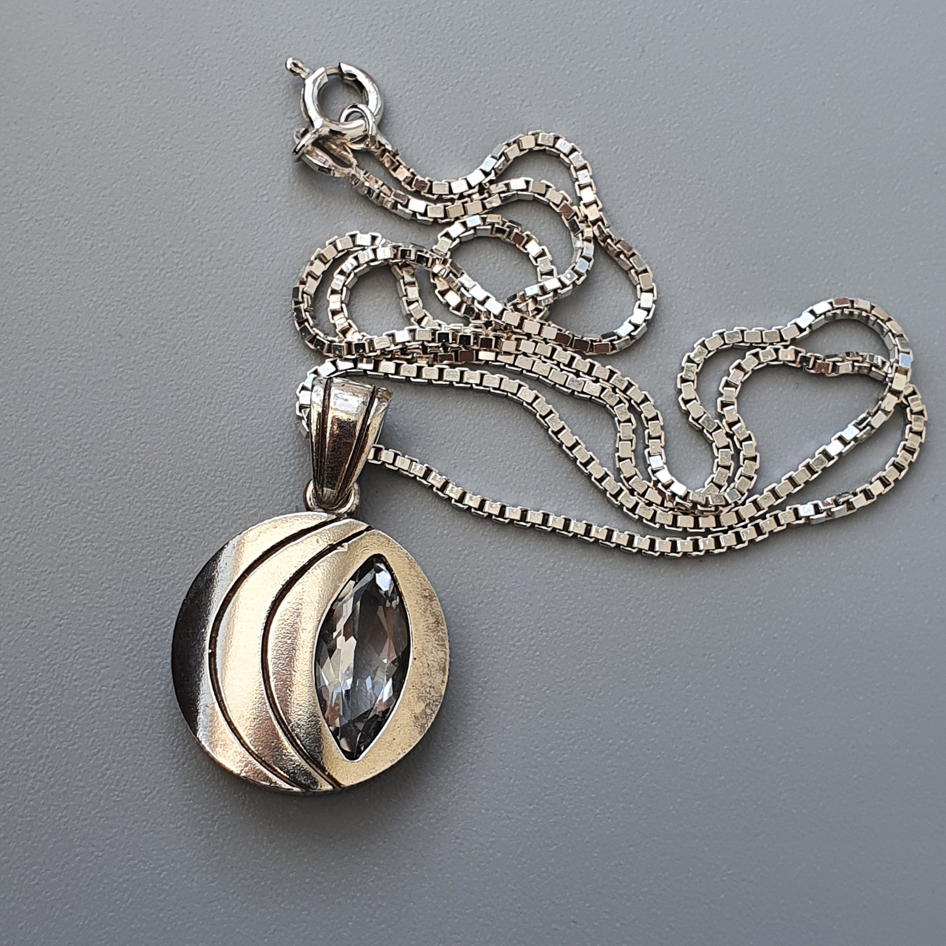 Silver pendant necklace featuring a circular charm with a marquise-cut gemstone.