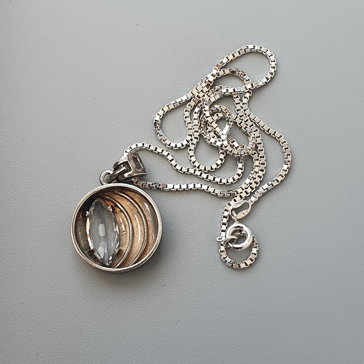 Pendant necklace with a circular glass locket containing copper-colored rings.