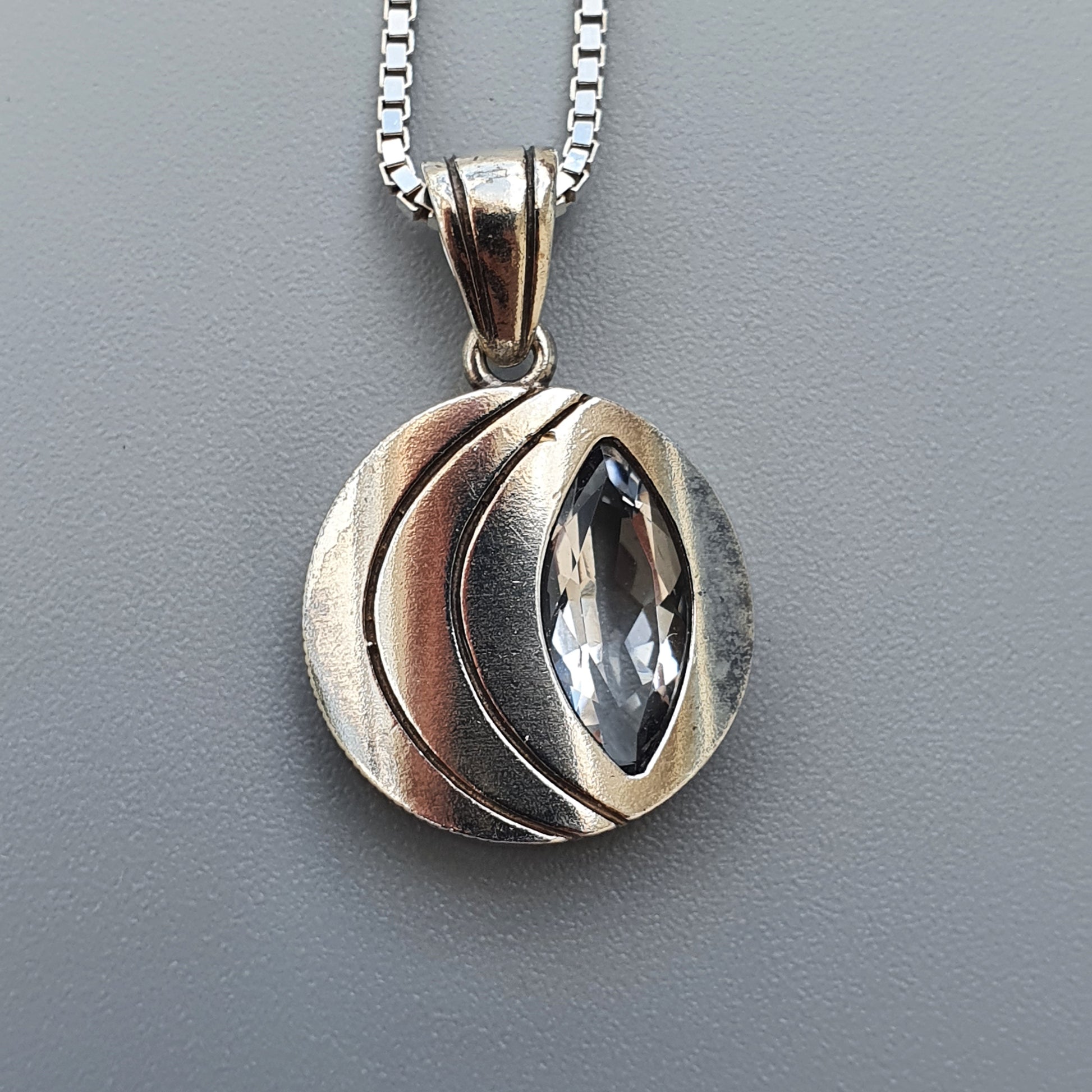 Silver pendant necklace featuring a circular design with a marquise-shaped gemstone.