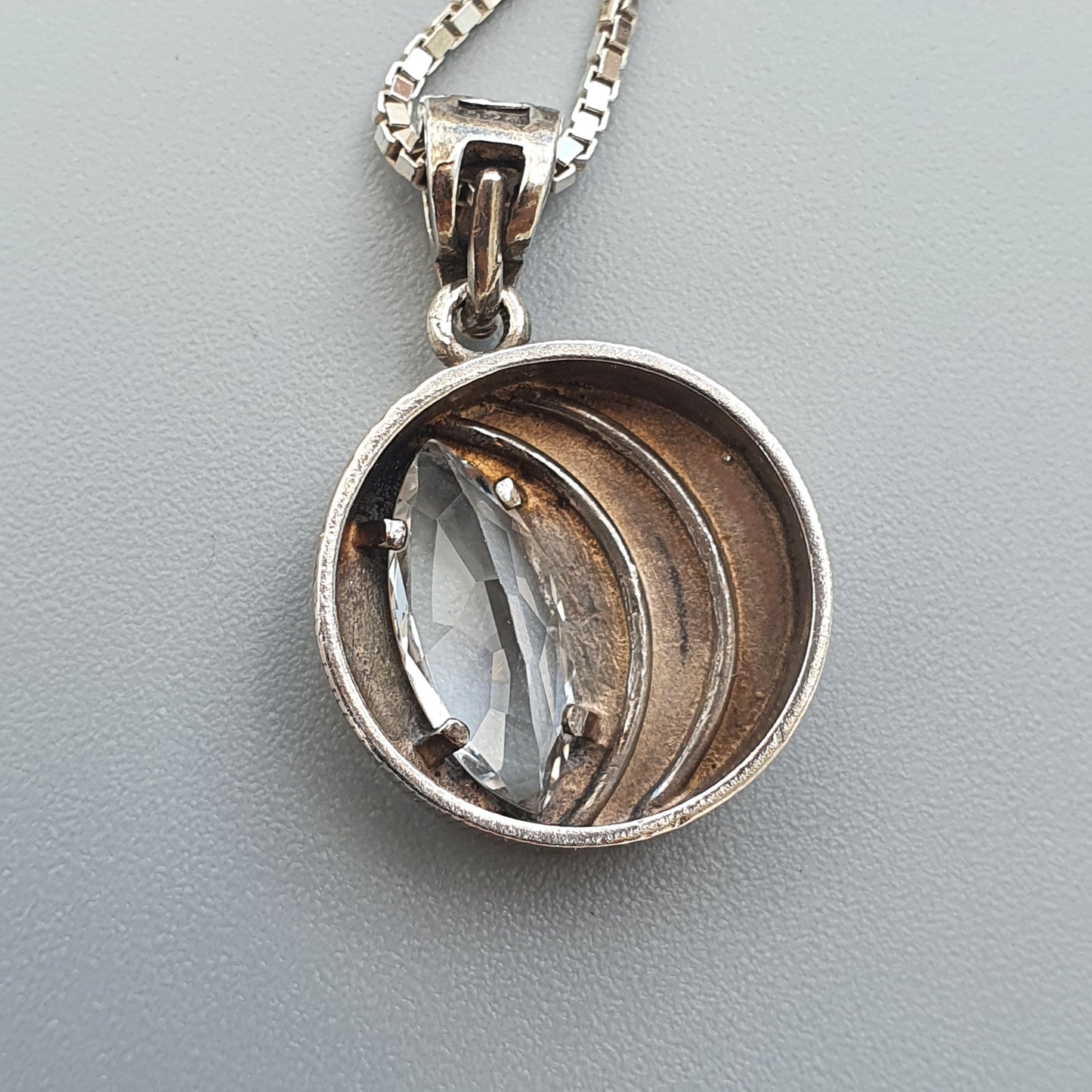 Silver pendant necklace featuring a circular design with a clear gemstone set within curved metal bands.