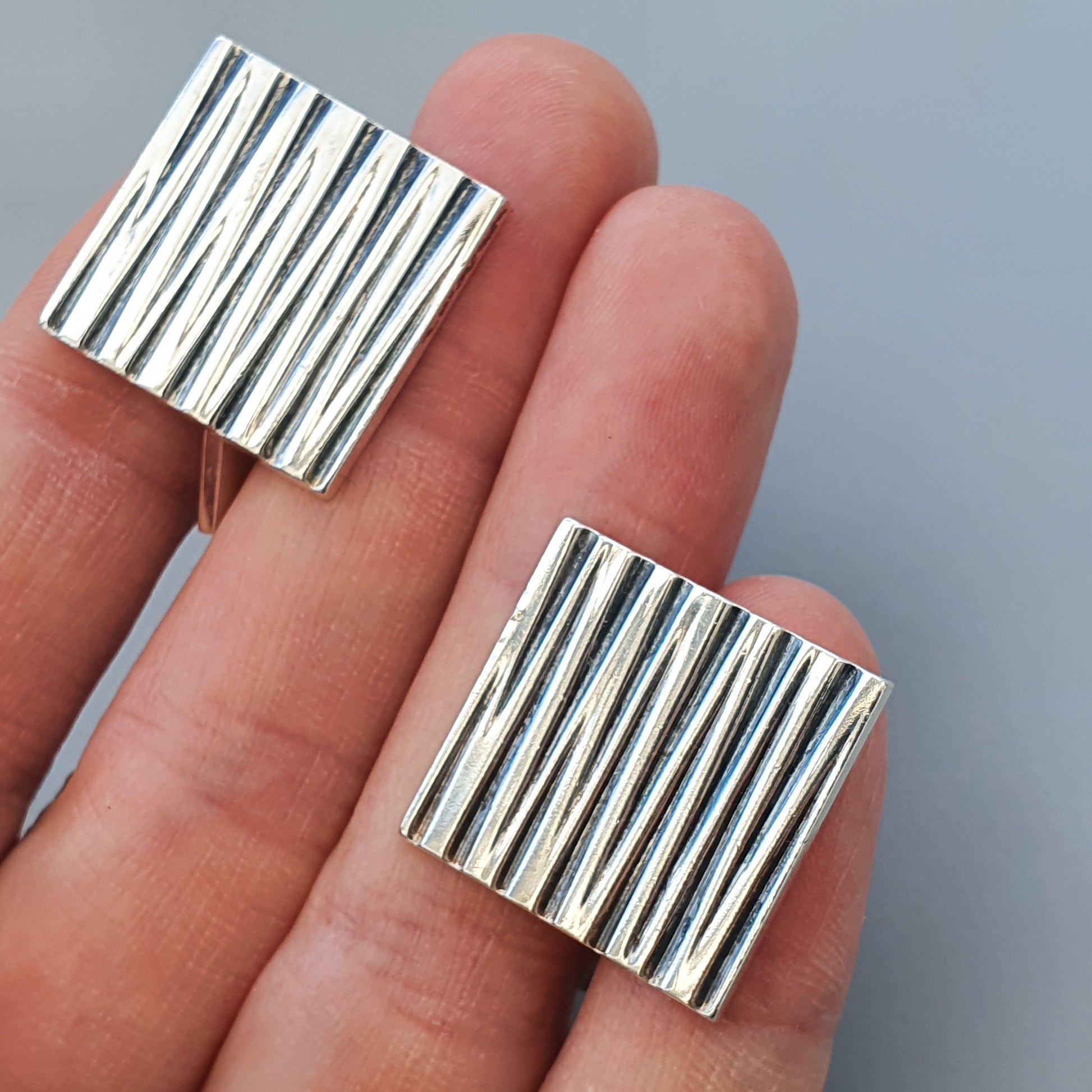 Pair of square silver earrings with vertical ridged patterns.