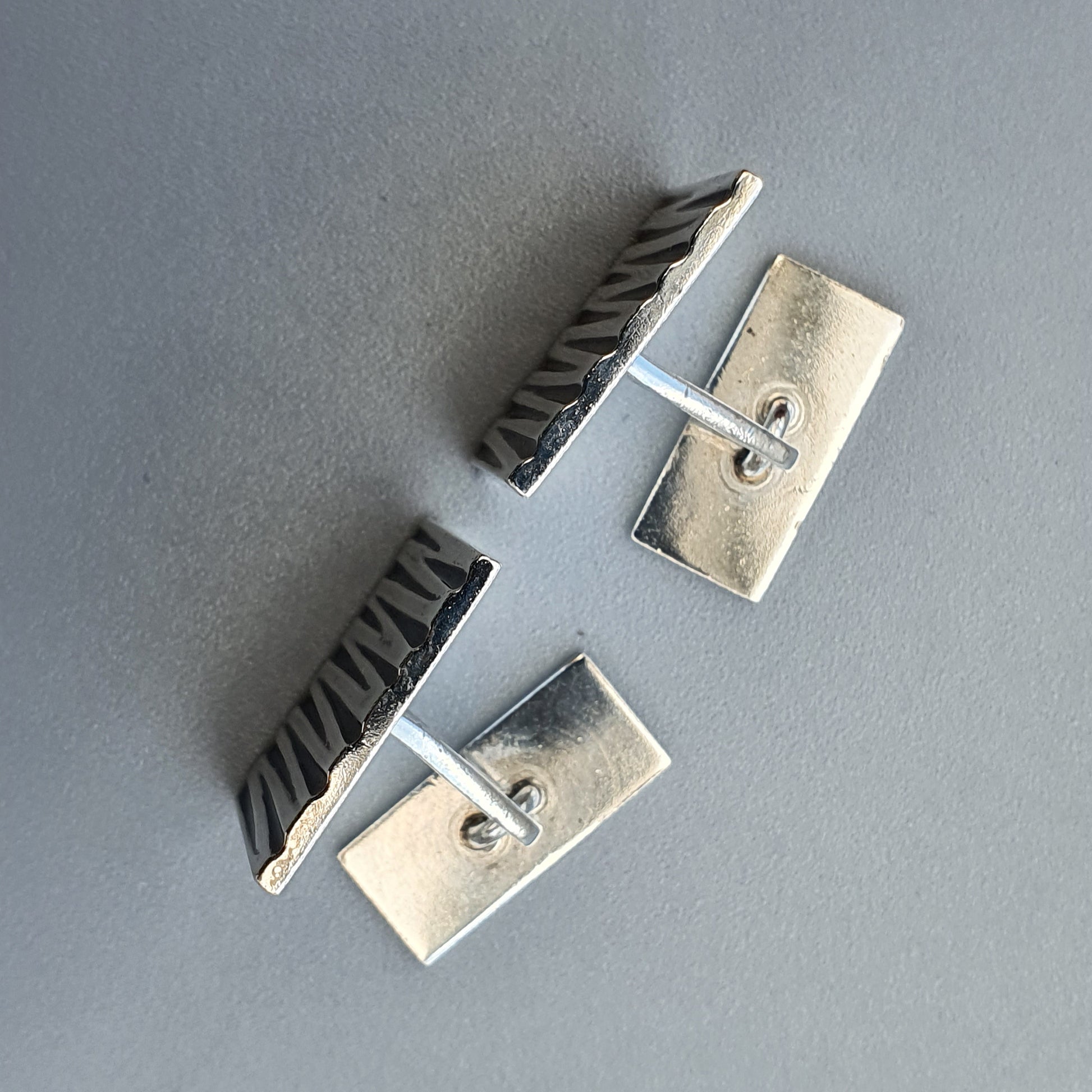 Metallic cufflink with brushed silver rectangular plates and a textured bar connecting them.