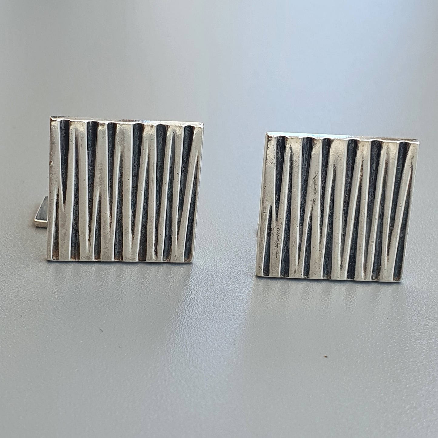 Pair of square silver cufflinks with vertical striped patterns.