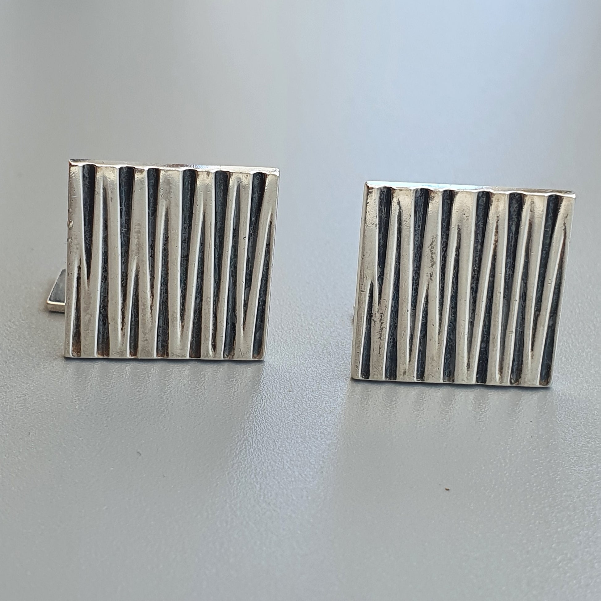 Pair of square silver cufflinks with vertical striped patterns.