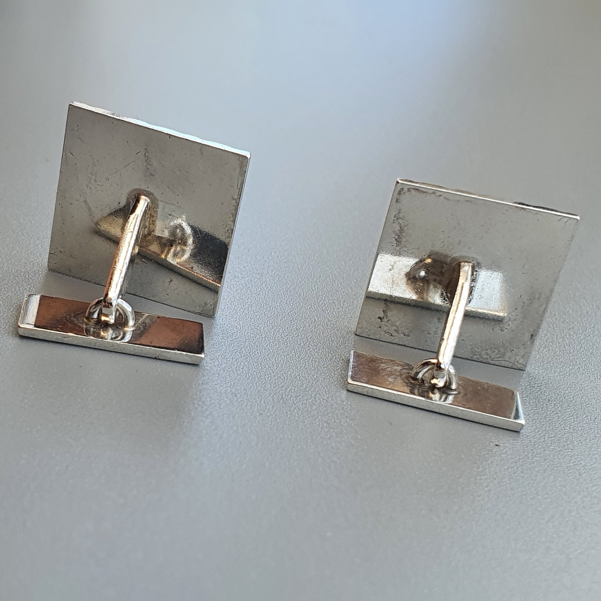 Pair of silver-colored square cufflinks with hinged backs.