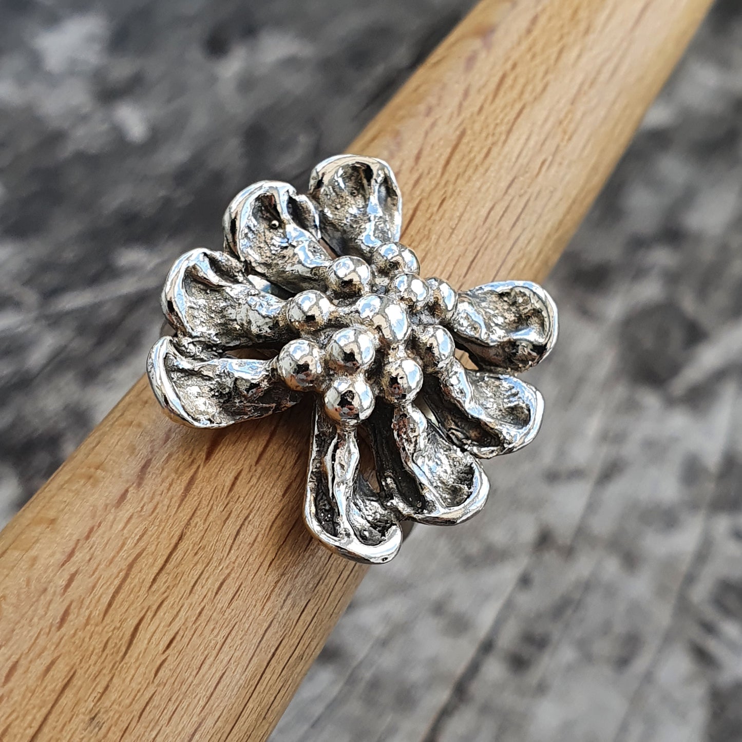 Silver flower-shaped ring with textured petals and a cluster of small beads in the center.