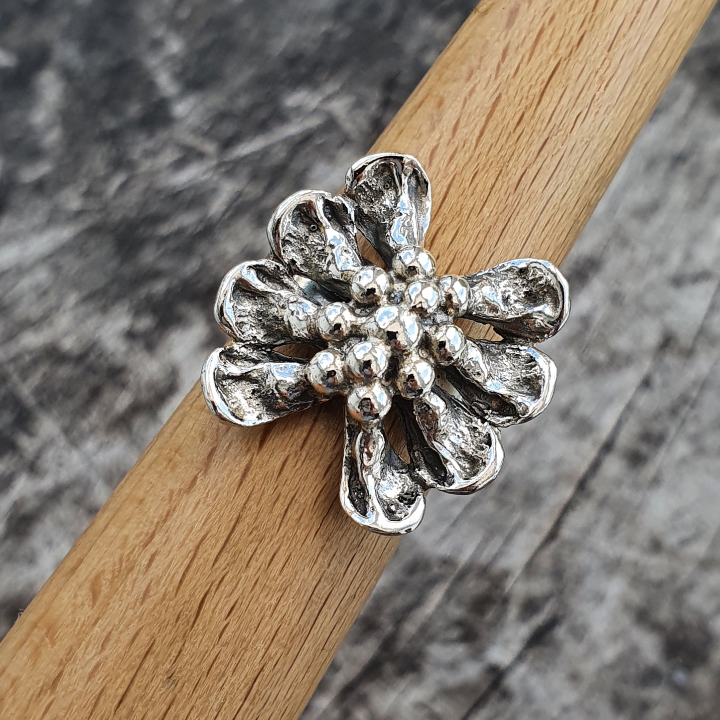 Silver flower-shaped ring with textured petals and a beaded center.