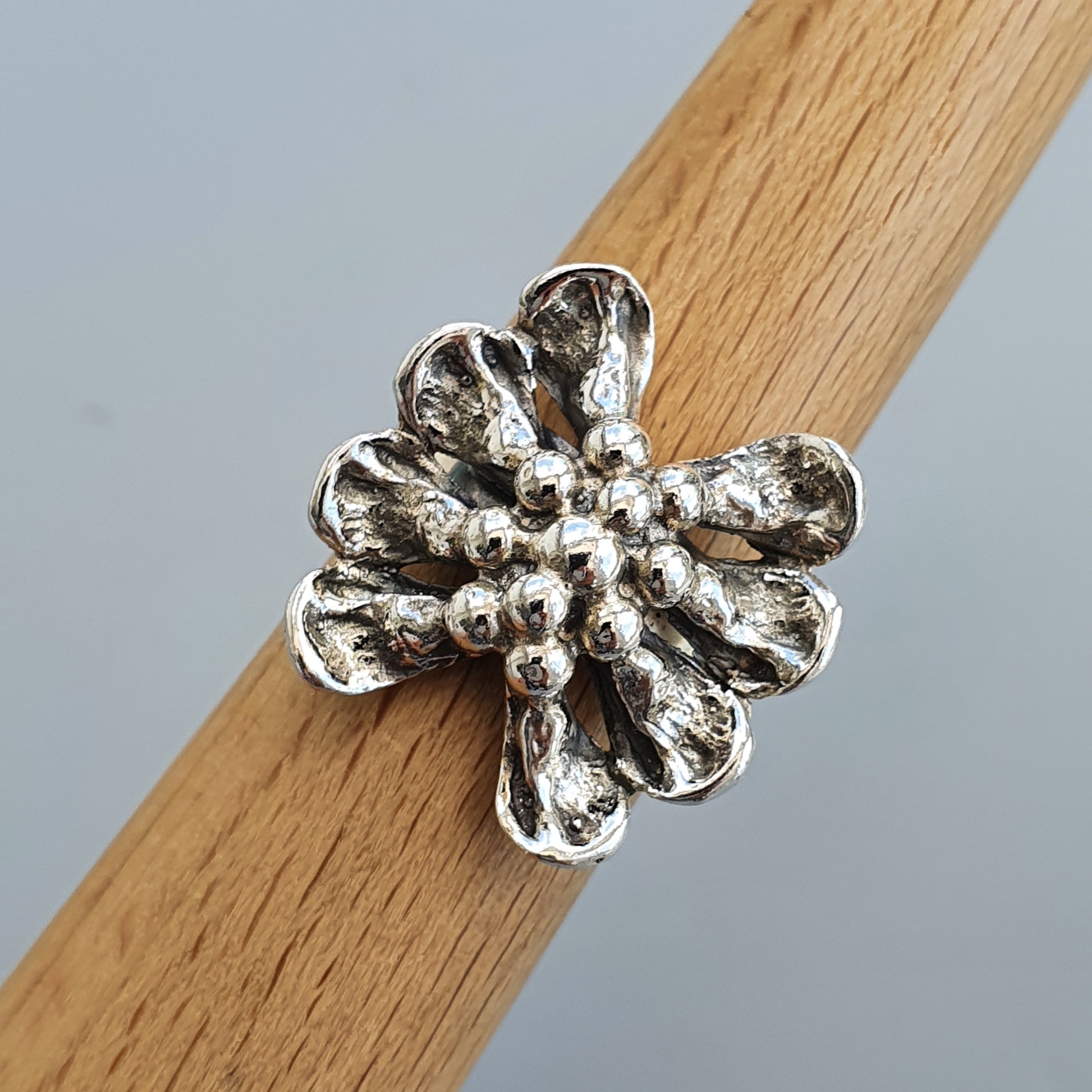 Silver flower-shaped ring with textured petals and a beaded center.