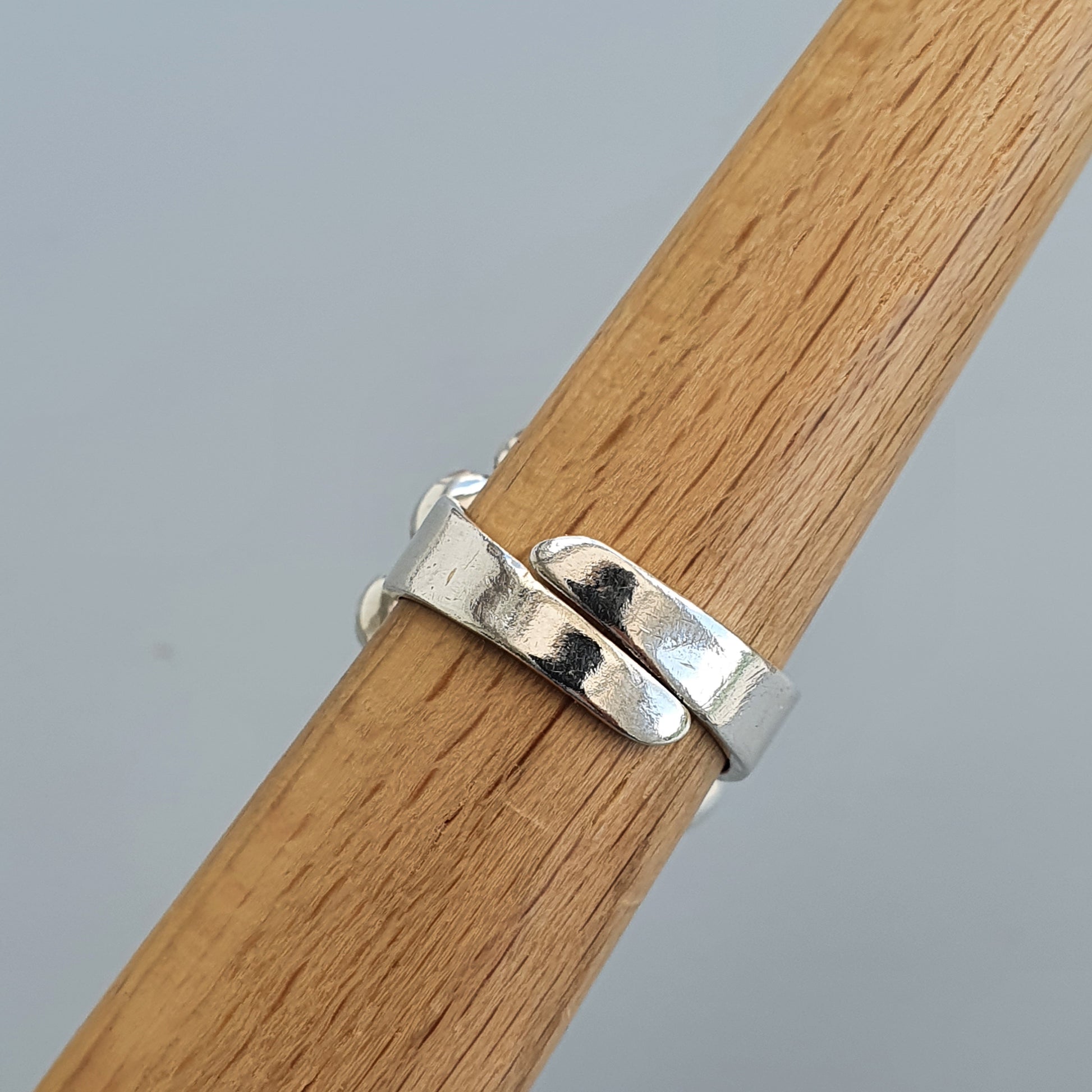 Silver ring with a wavy or undulating design wrapped around a wooden surface.