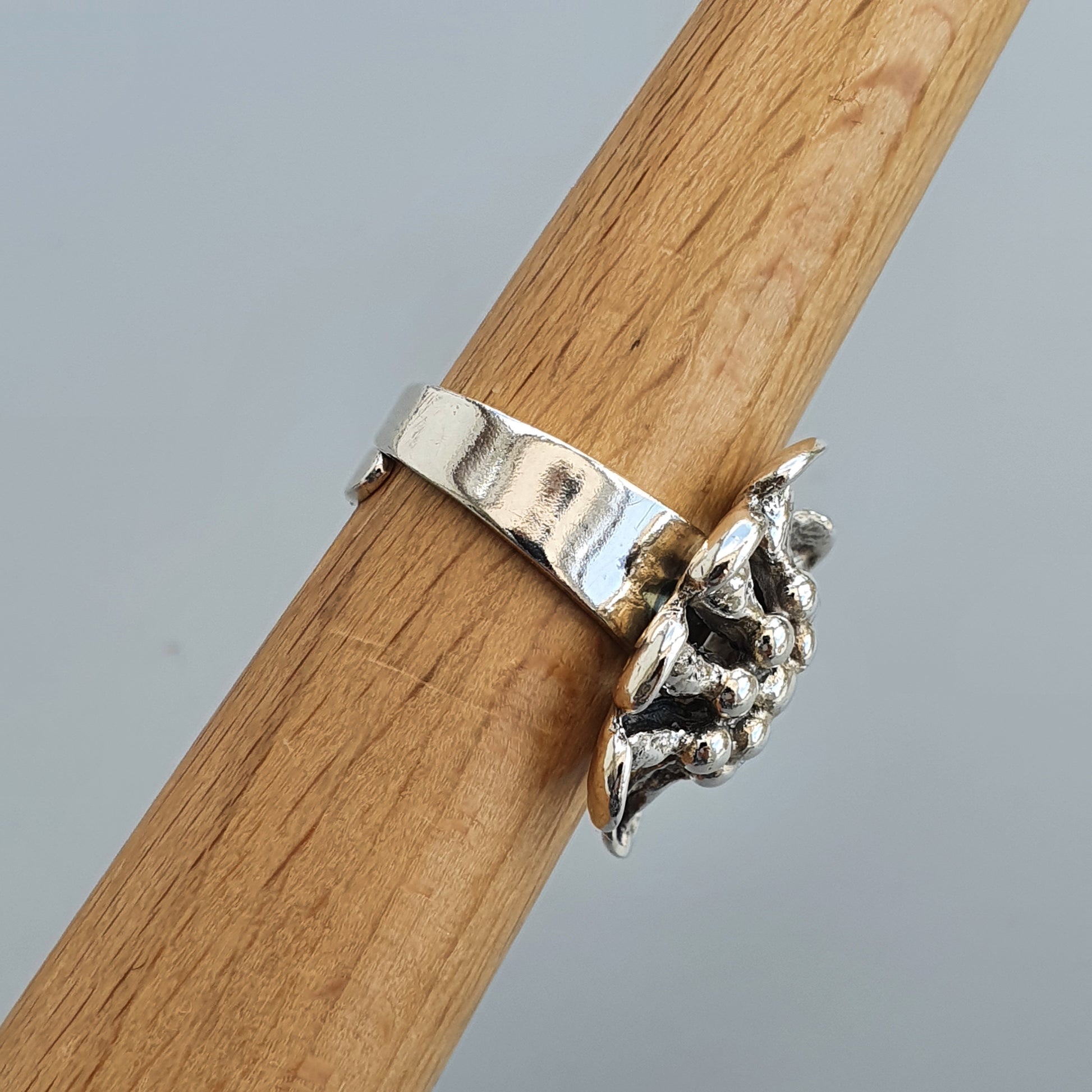 Silver ring with an intricate leaf or floral design wrapped around a wooden surface.