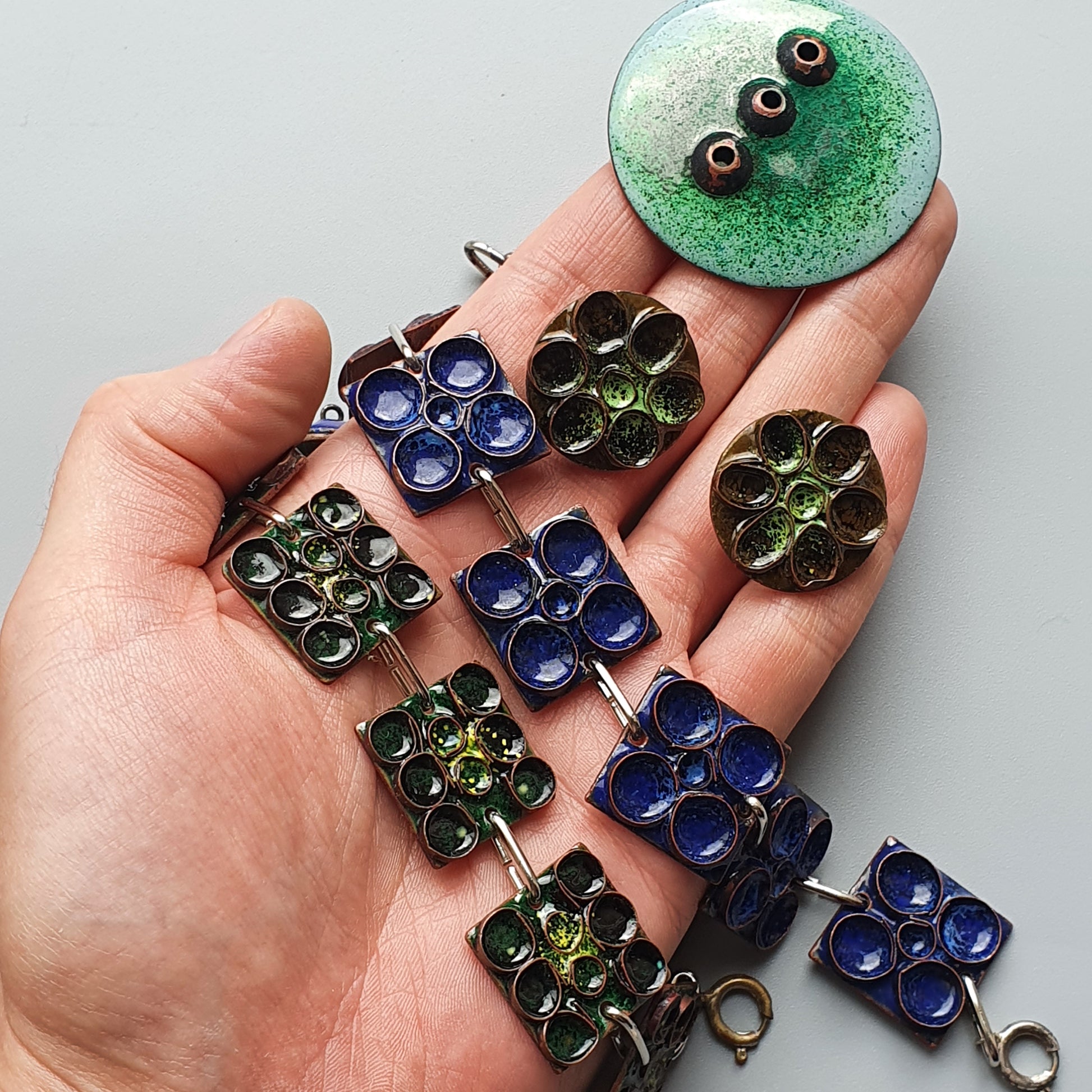 Hand holding various glass pendants and jewelry pieces in green and blue colors.