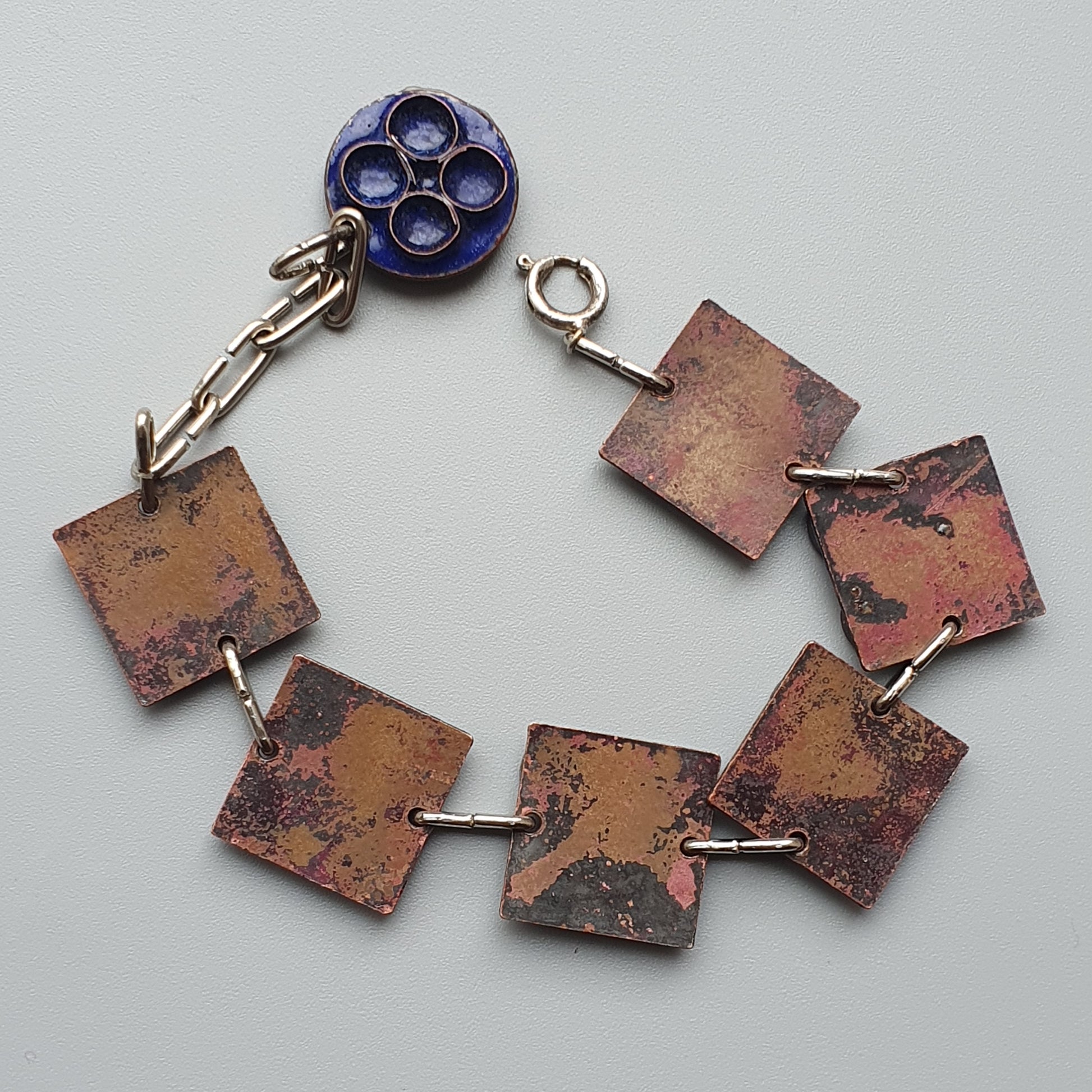 Handmade bracelet with rustic copper-colored square links and a blue circular clasp.