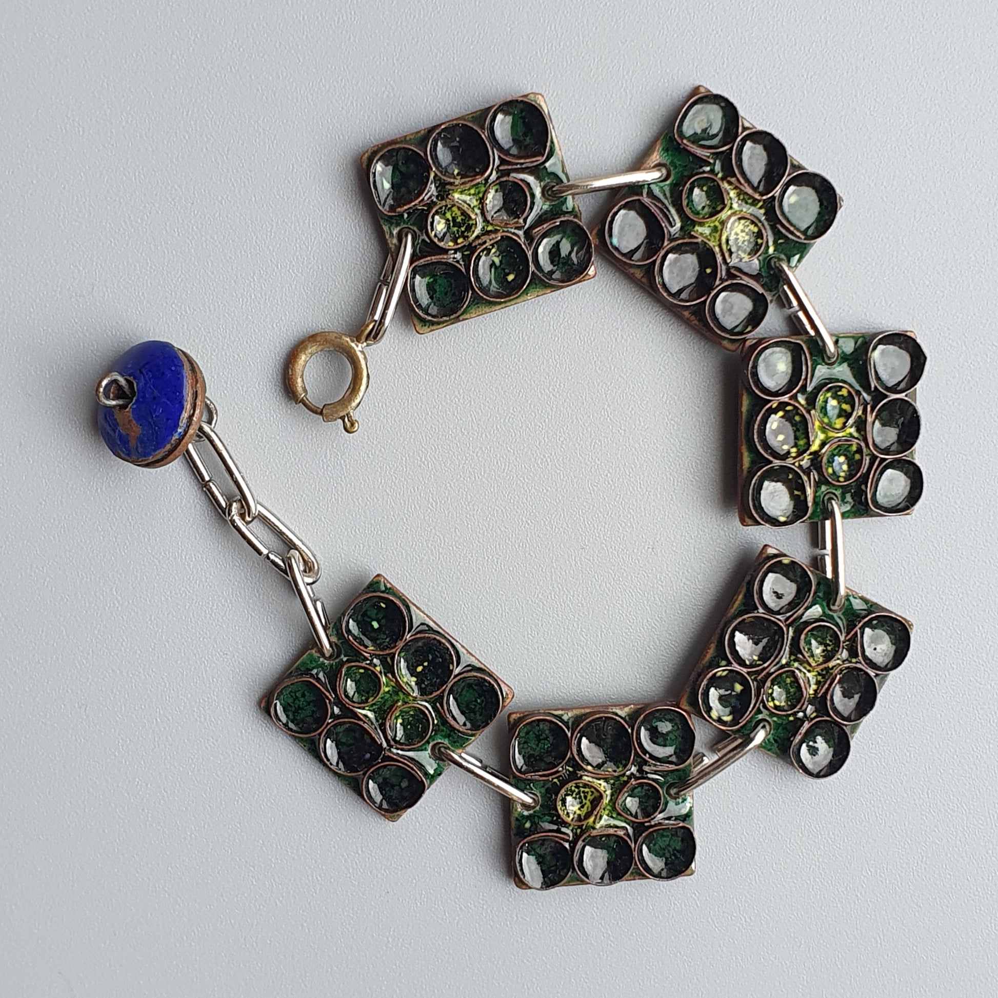 Ornate bracelet with square links containing green and dark gemstones.