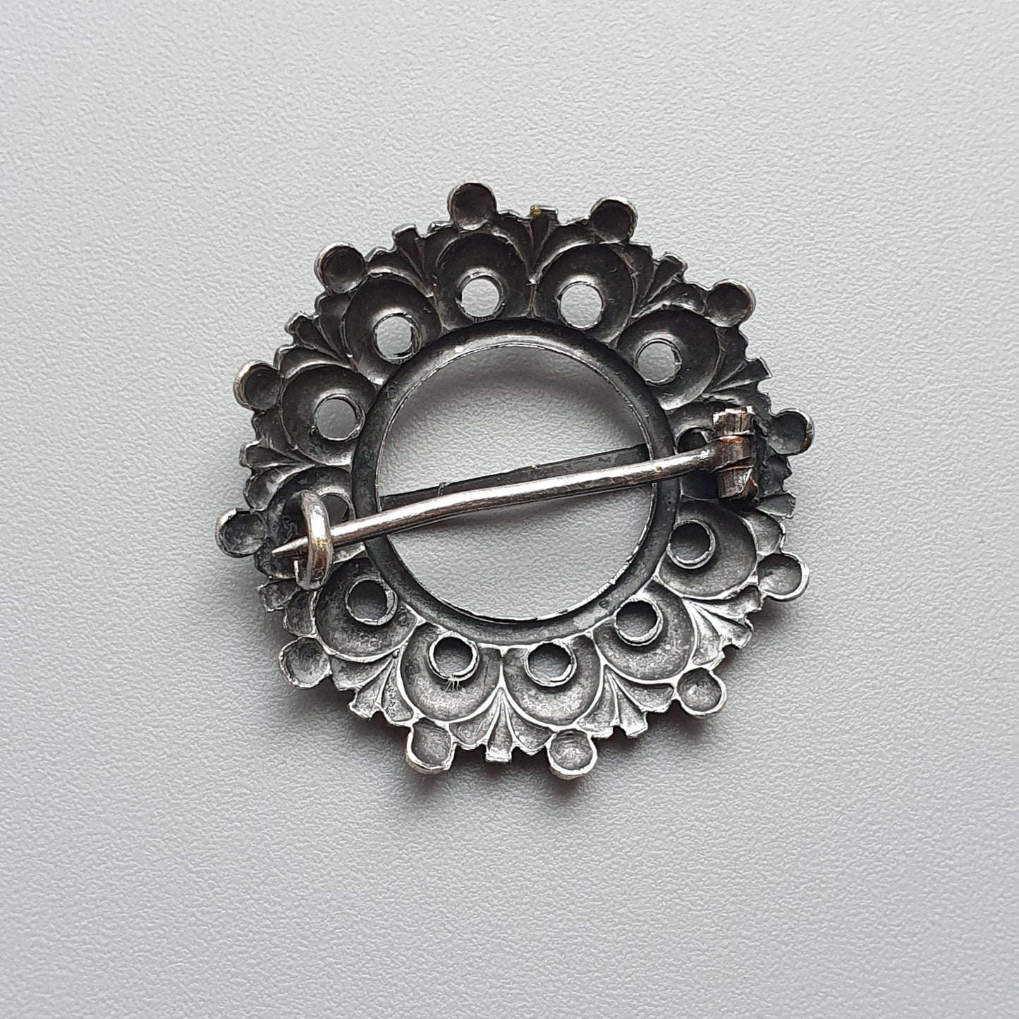 Ornate circular silver brooch with intricate filigree patterns and a central pin.