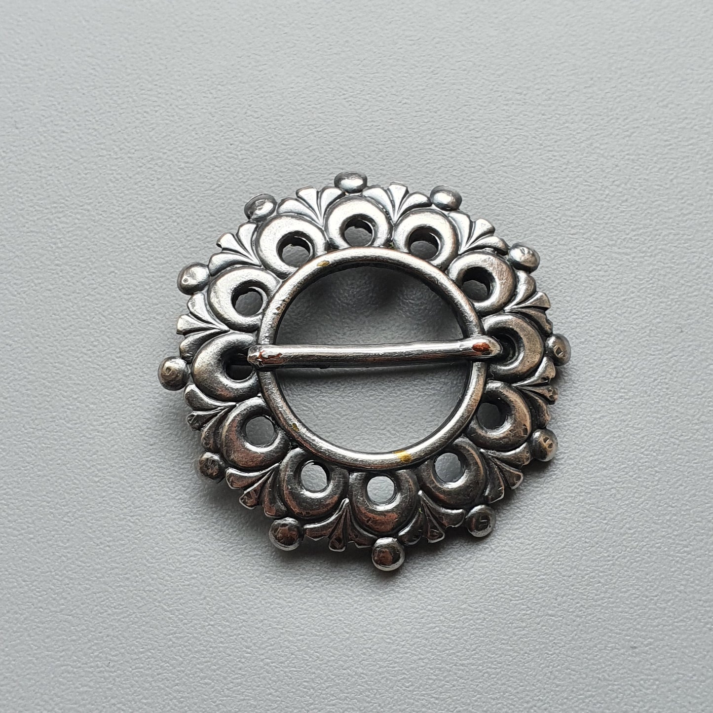 Ornate silver brooch with a circular design featuring floral and peacock-like patterns.