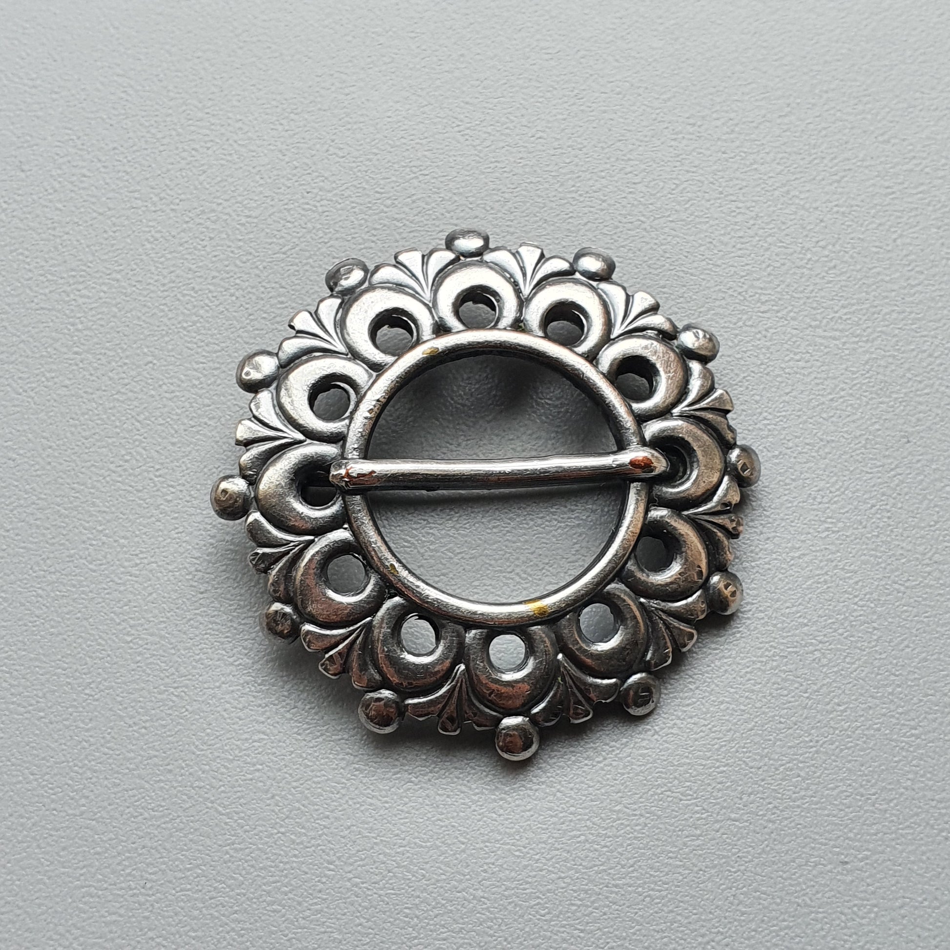 Ornate silver brooch with a circular design featuring floral and peacock-like patterns.