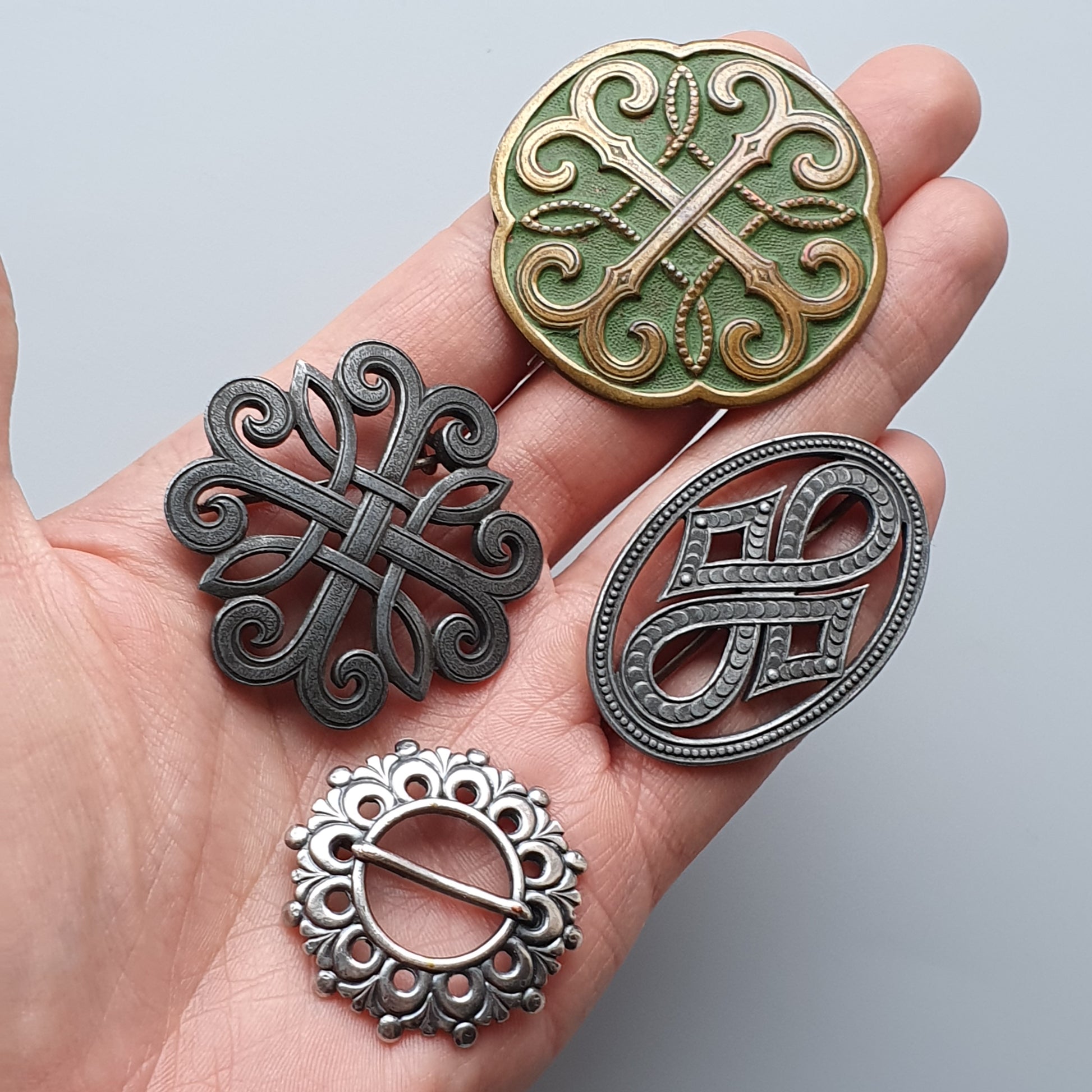 Hand holding four decorative metal brooches or pendants with intricate Celtic-inspired designs.