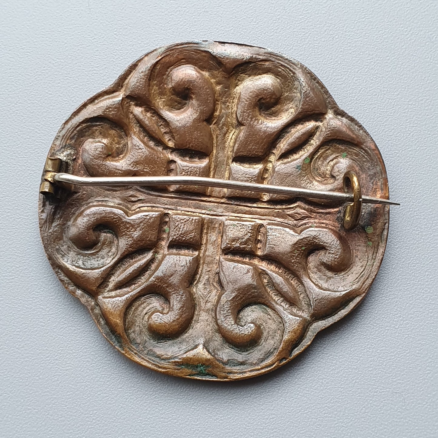 Ornate circular bronze brooch with intricate spiral patterns and a central pin.