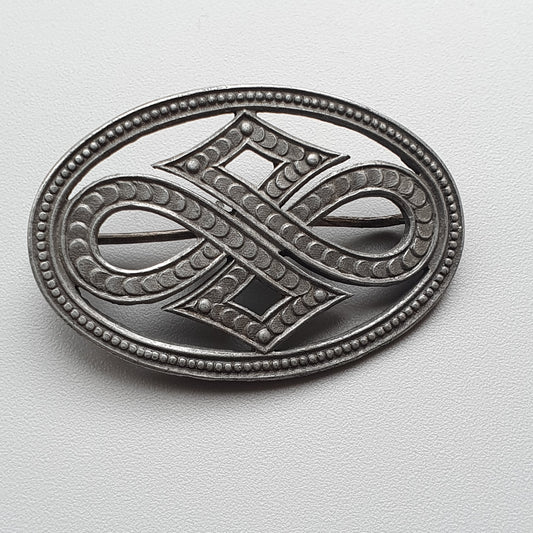 Ornate metal brooch or pendant with an intricate infinity-like design.