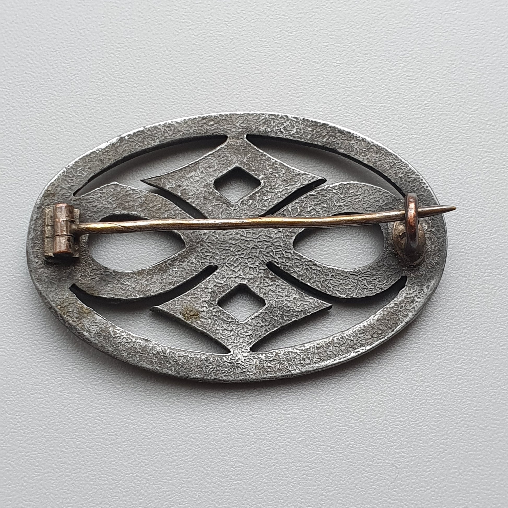 Oval-shaped metal brooch with intricate geometric design and a pin fastener.